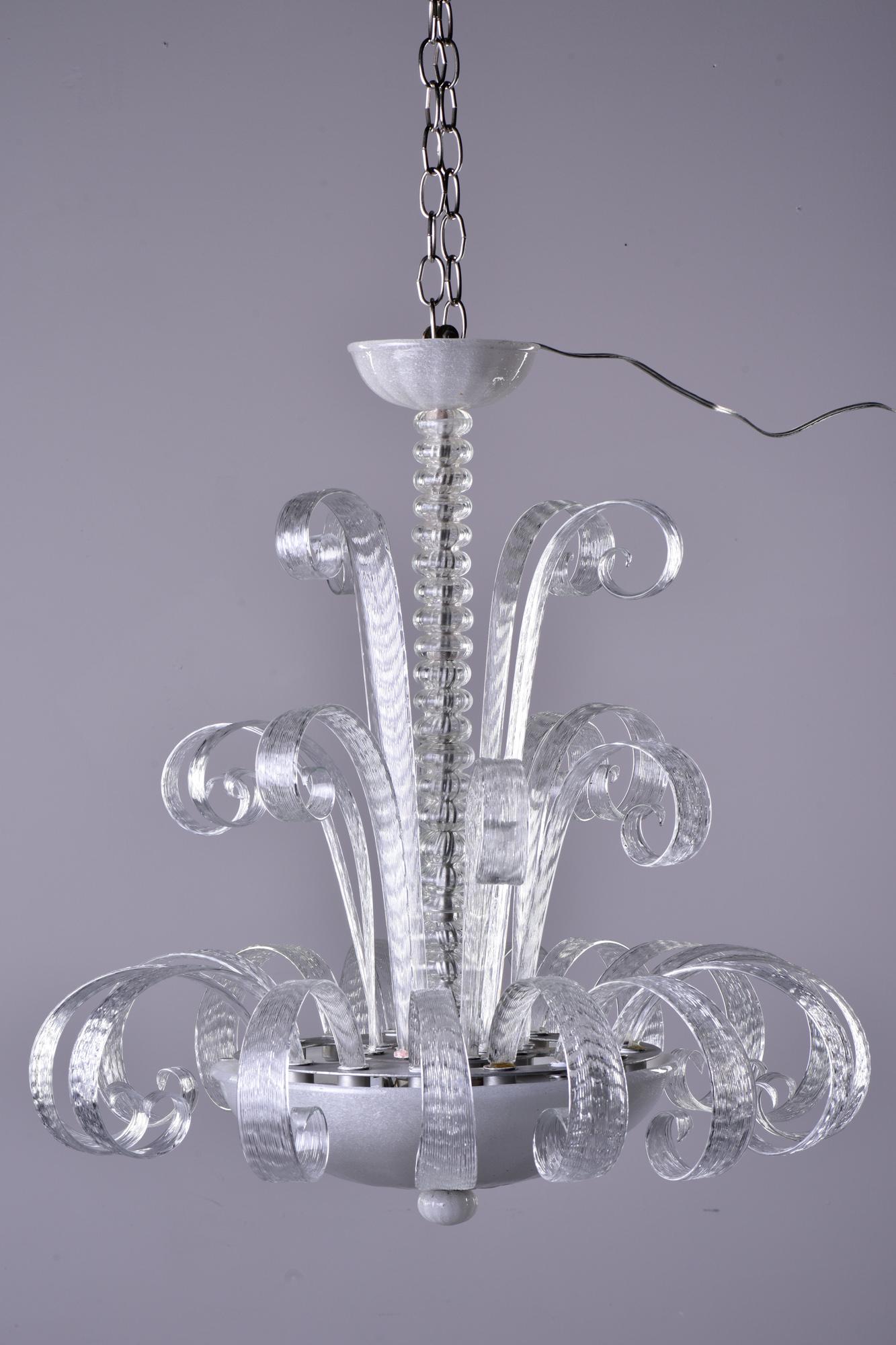 Circa 1940s clear Murano glass chandelier features a center bowl with four sockets and three tiers of curvy glass stems and a glass ceiling canopy. Unknown Murano maker. Rewired for US electrical standards.