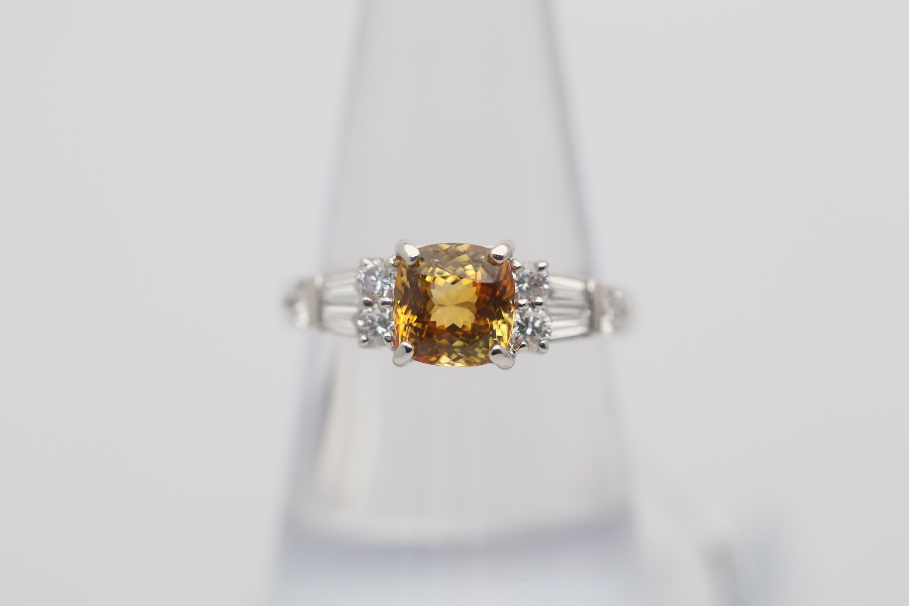 A sweet and stylish ring featuring a 2.00 carat fancy colored sapphire with a vibrant orange-yellow color. It has a brilliant cushion-shape giving the stone excellent scintillation and light return. It is complemented by 0.62 carats round-brilliant