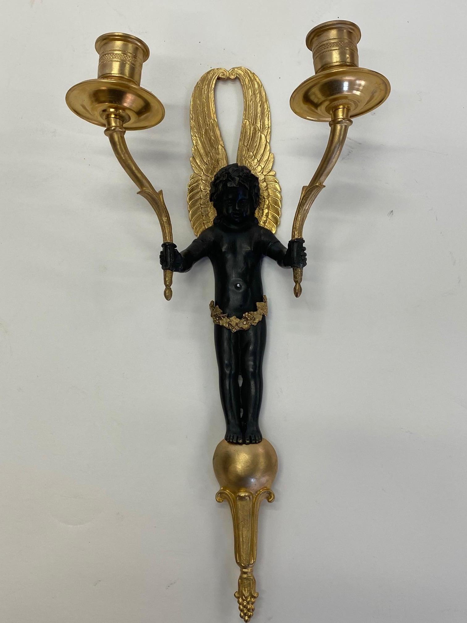 Ornate early 20th century pair of candle wall sconces having gold on bronze and patinated bronze finish to the putti figures with gold wings and dramatic poses.