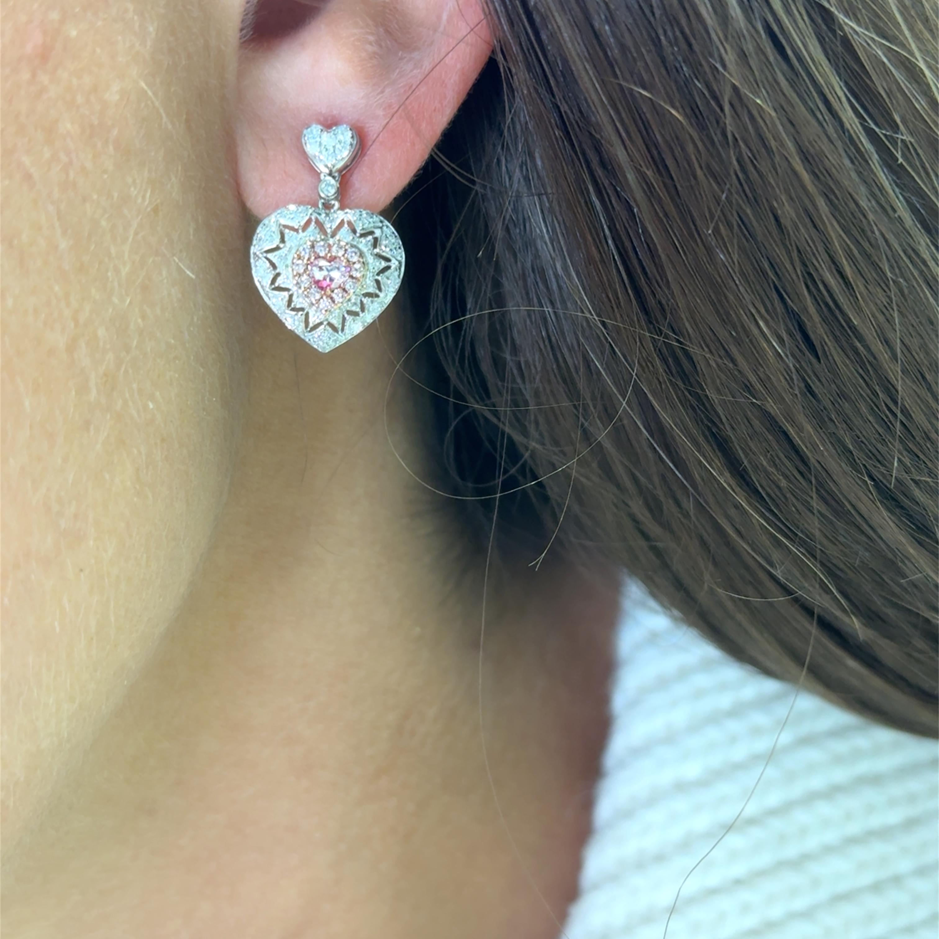 Indulge in the captivating allure of these 18k white gold dangle drop earrings, showcasing heart-shaped fancy pink diamonds. The brilliant-cut diamonds emit a mesmerizing sparkle, complemented by the 18k white gold setting. These earrings exude