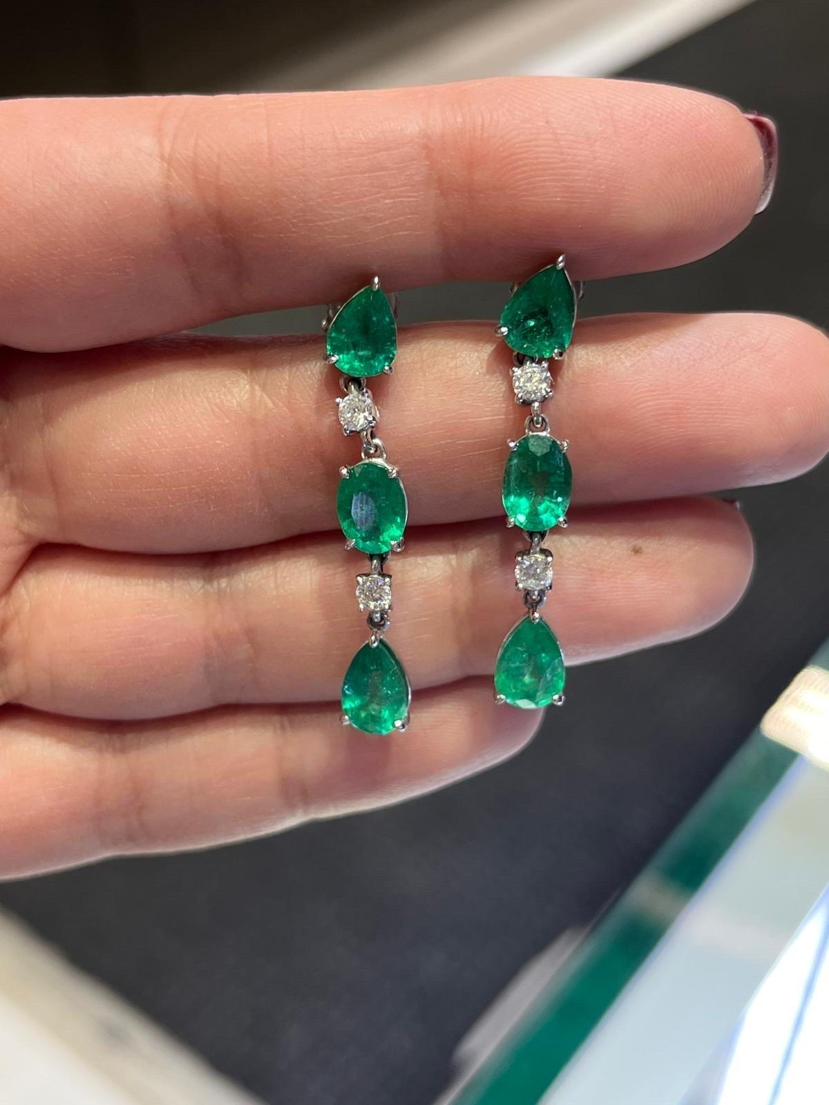 Hängende Ohrringe aus kolumbianischem Smaragd und Diamant in 14 Karat Weißgold. Die Ohrringe sind mit ovalen und birnenförmigen grünen Smaragdsteinen und 4 runden Diamanten besetzt. Das Karatgewicht der 6 Smaragde beträgt 6,06 und das der Diamanten