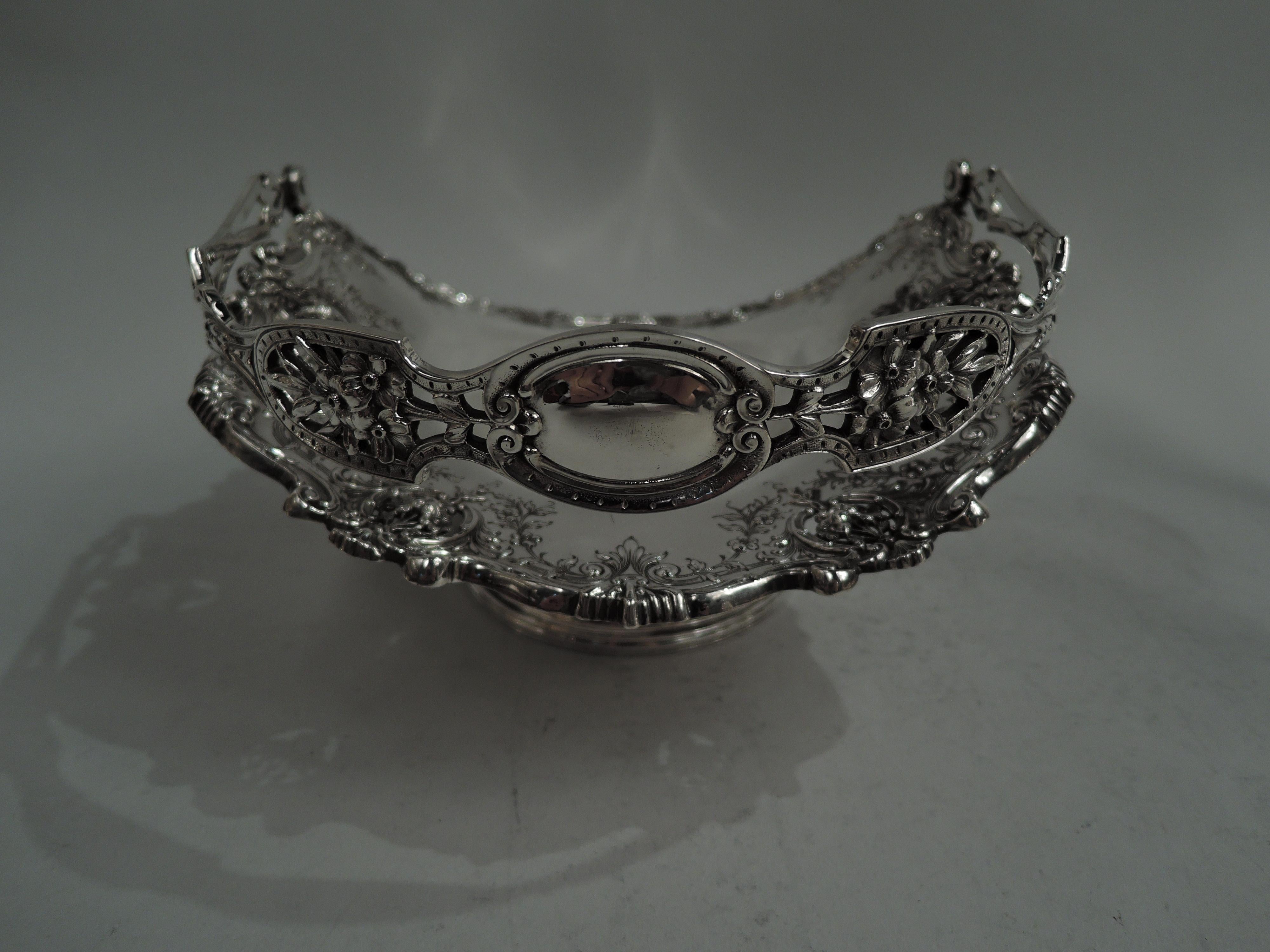 Fancy American Victorian sterling silver basket, ca 1890. Retailed by Tiffany & Co. in New York. Oval well and wide flared mouth; spread and reeded foot. Rim interior has cast scrolls, shells, and leaves with pendant flowers in open scroll rondels