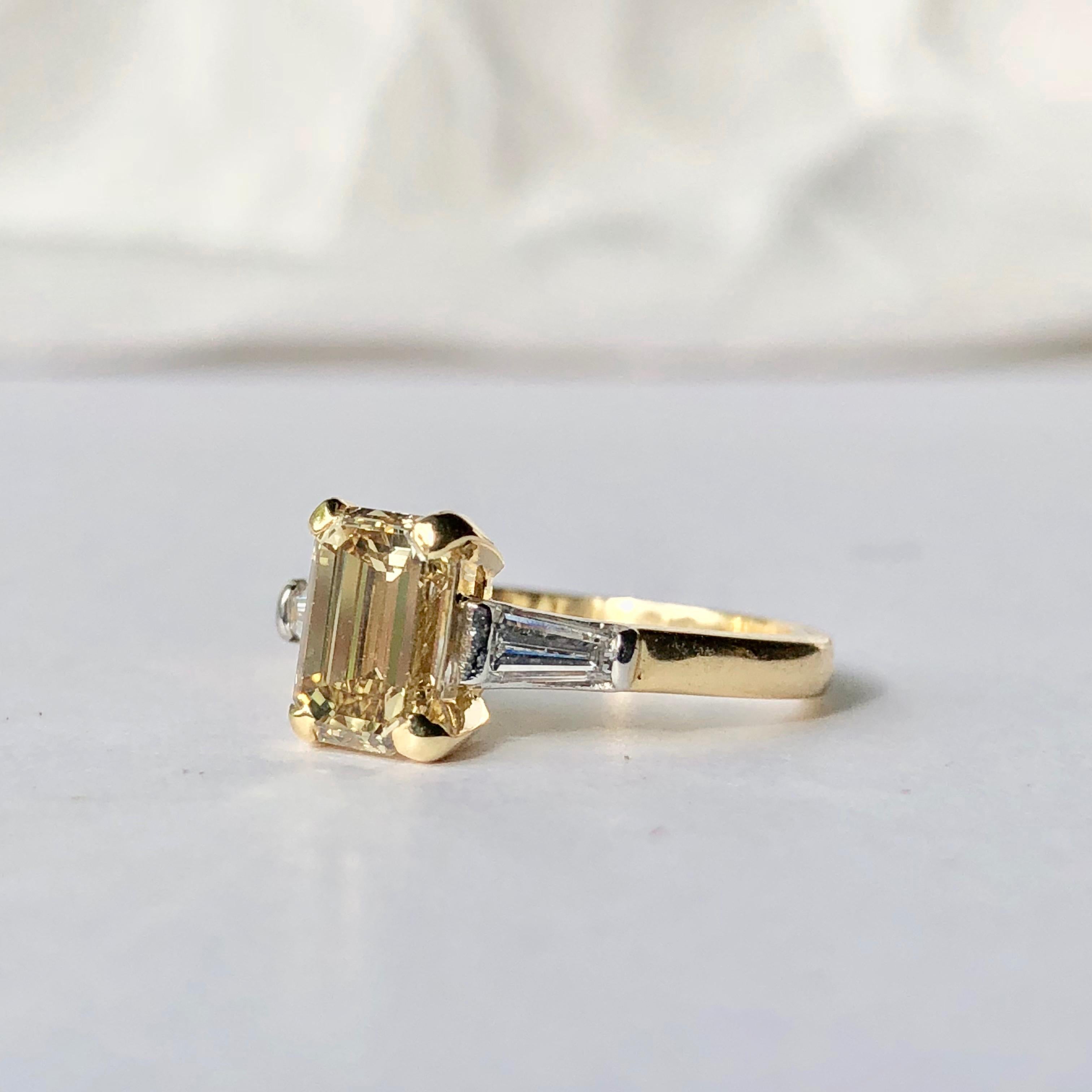 An Elegant Step Cut Yellow Diamond Ring 

The Principal Diamond Set In 18K Yellow Gold Four Claw Setting With White Tapered Baguette Diamond Shoulder Stones.

The Yellow Diamond is VS Clarity  and Weighs An Estimated 1.01cts With 0.26ct White