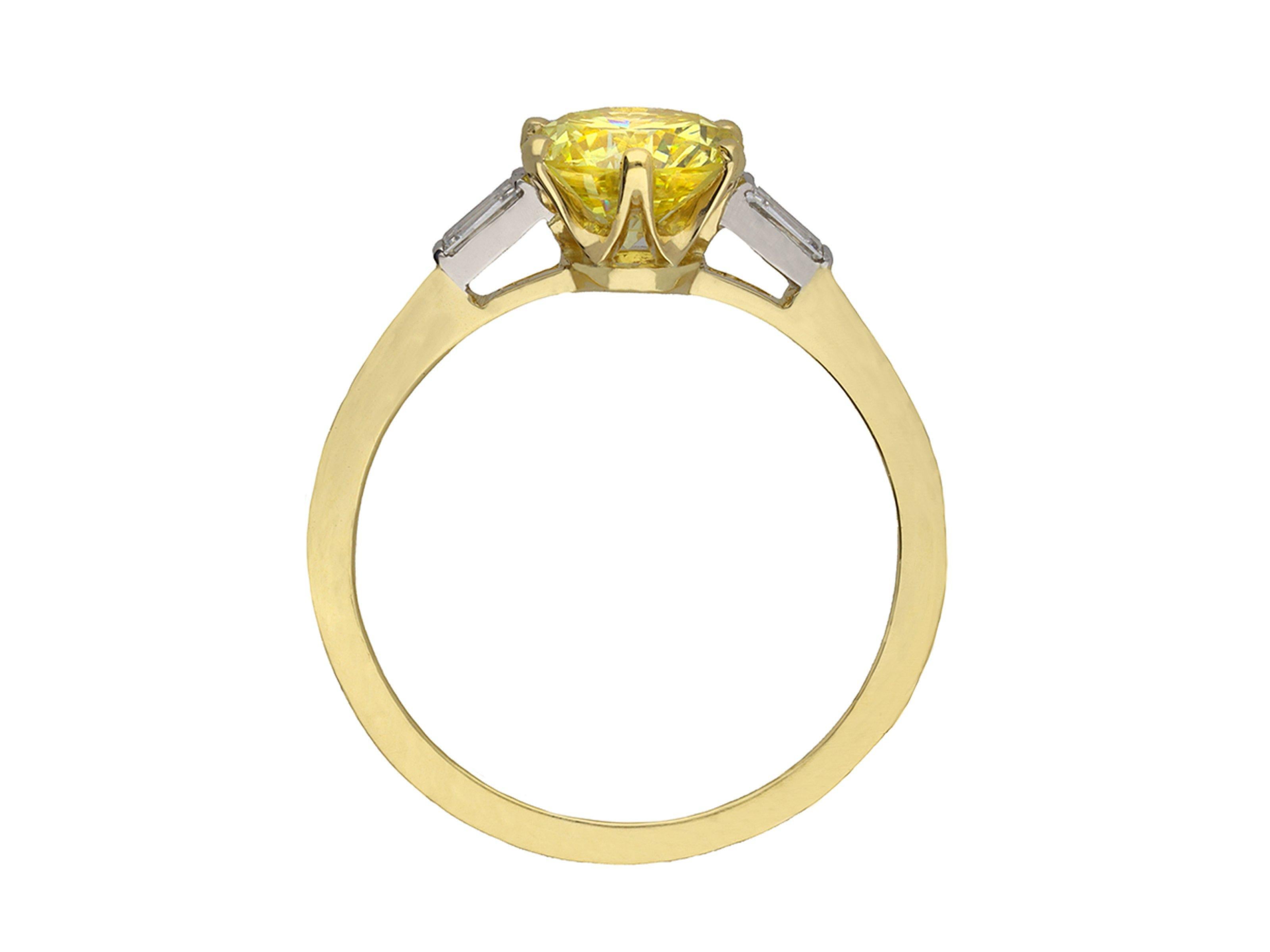 Fancy yellow diamond flanked solitaire ring. Set to center with a round transitional cut natural unenhanced fancy intense yellow diamond, SI2 clarity, with a weight of 1.10 carats, in open back claw settings, flanked by two tapered baguette cut