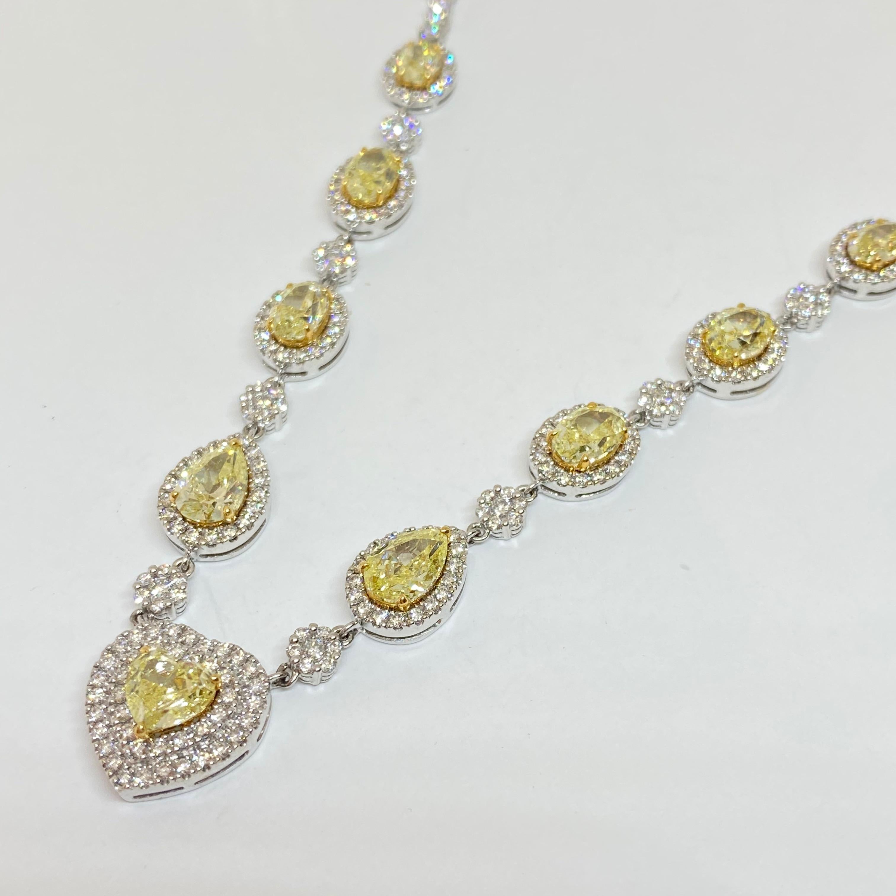 This one-of-a-kind diamond riviera necklace features fancy yellow heart, pear and oval shape diamonds surrounded by white diamond halos. The necklace is designed in 18 karat white and yellow gold. The necklace measures 17