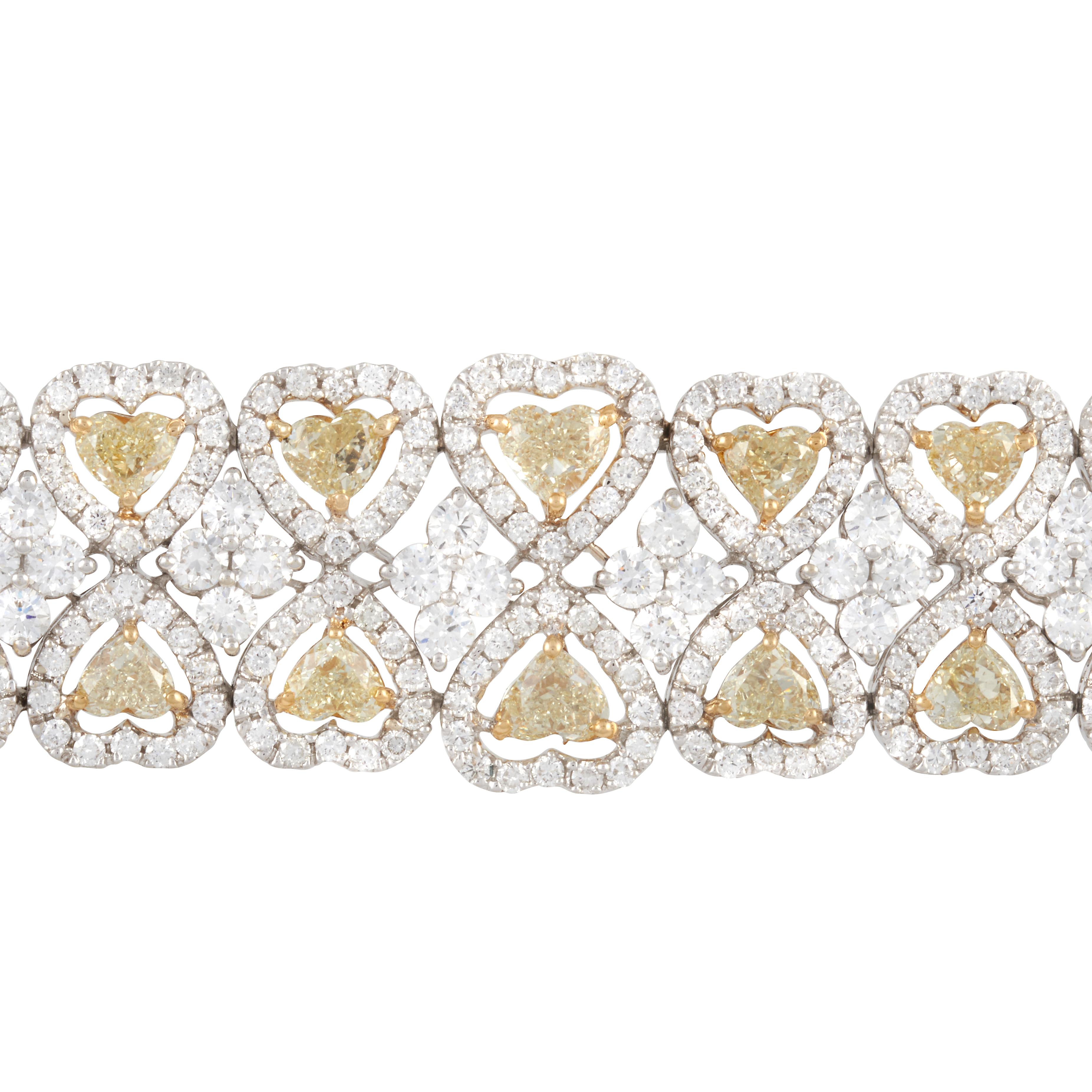 A 18-karat white and yellow gold diamond bracelet with two rows of heart shape diamonds with white diamond halos. There are 38 Fancy Yellow heart diamonds that weight about 13.50 carats with a VS clarity. There are 612 round white diamonds that