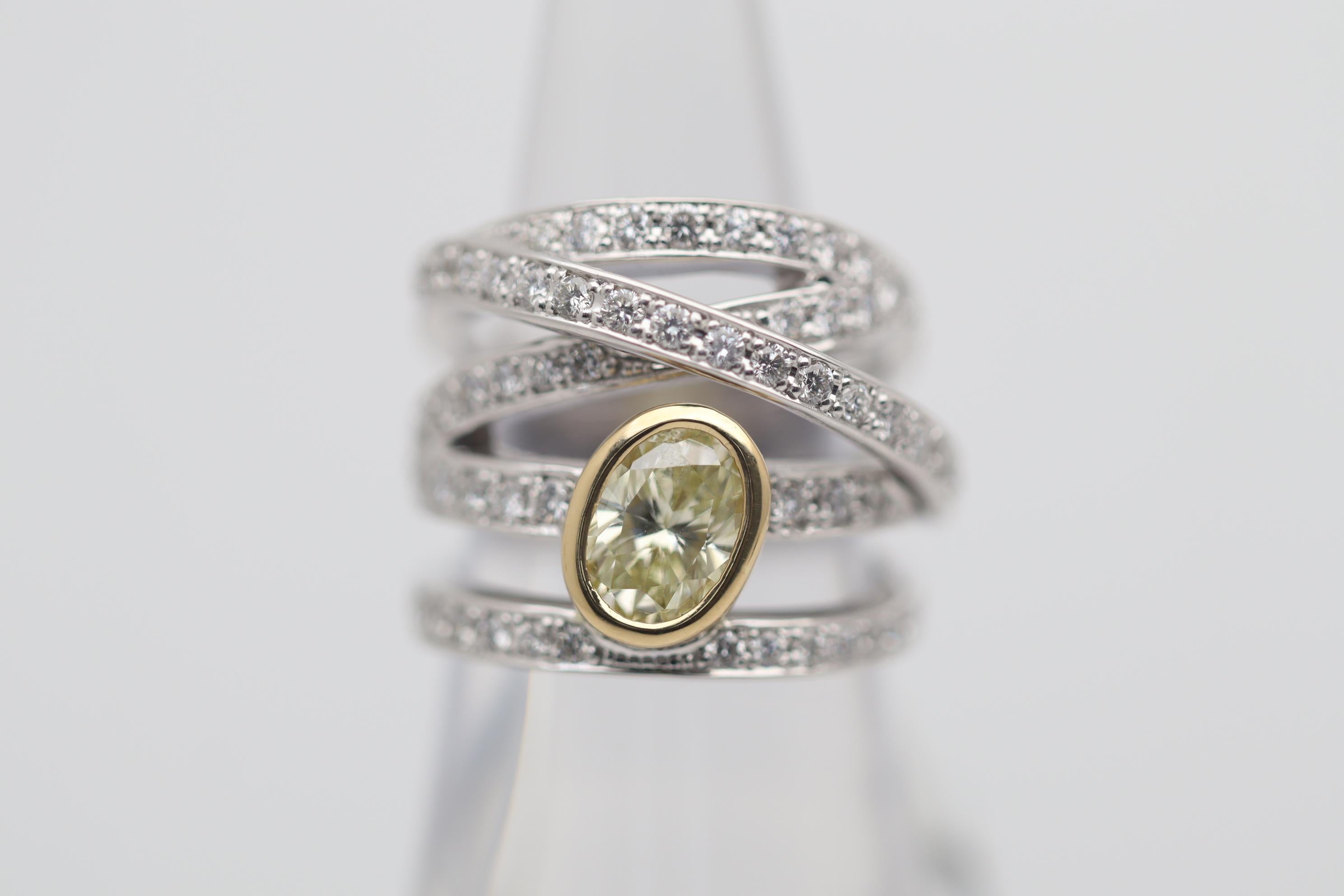 A fun and stylish ring featuring a 1.23 carat fancy yellow diamond. It has a beautiful oval shape and is bezel set in 18k yellow gold to help complement the stones natural color. Adding to that, are 1.18 carats of bright white round brilliant-cut