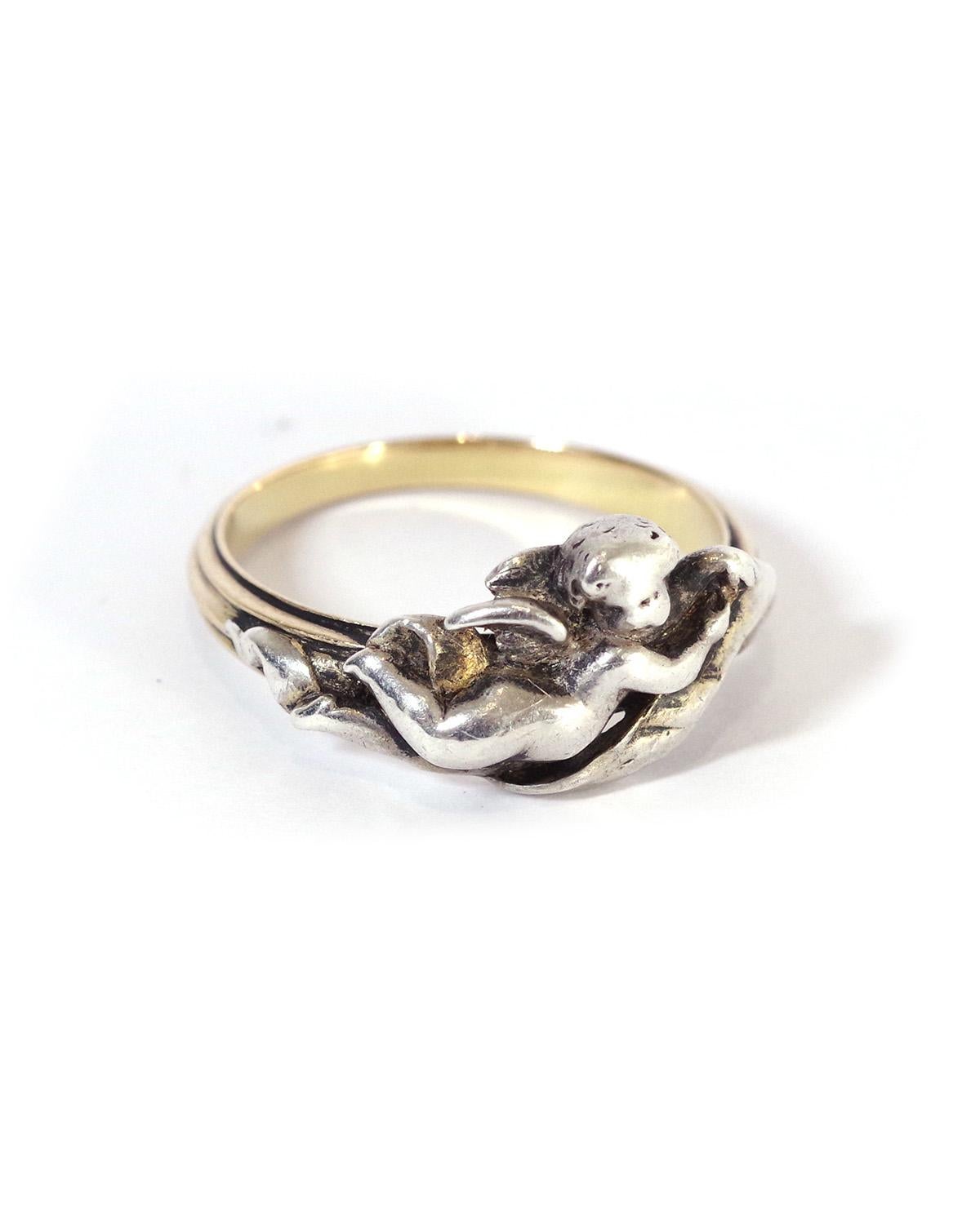 Fannière Frères angel ring in 18 karat gold and silver. Antique ring with charming decoration, depicting an angel holding a ribbon. The angel is in silver, mounted on a gold ring soberly decorated with fine striations. The ring is signed on the