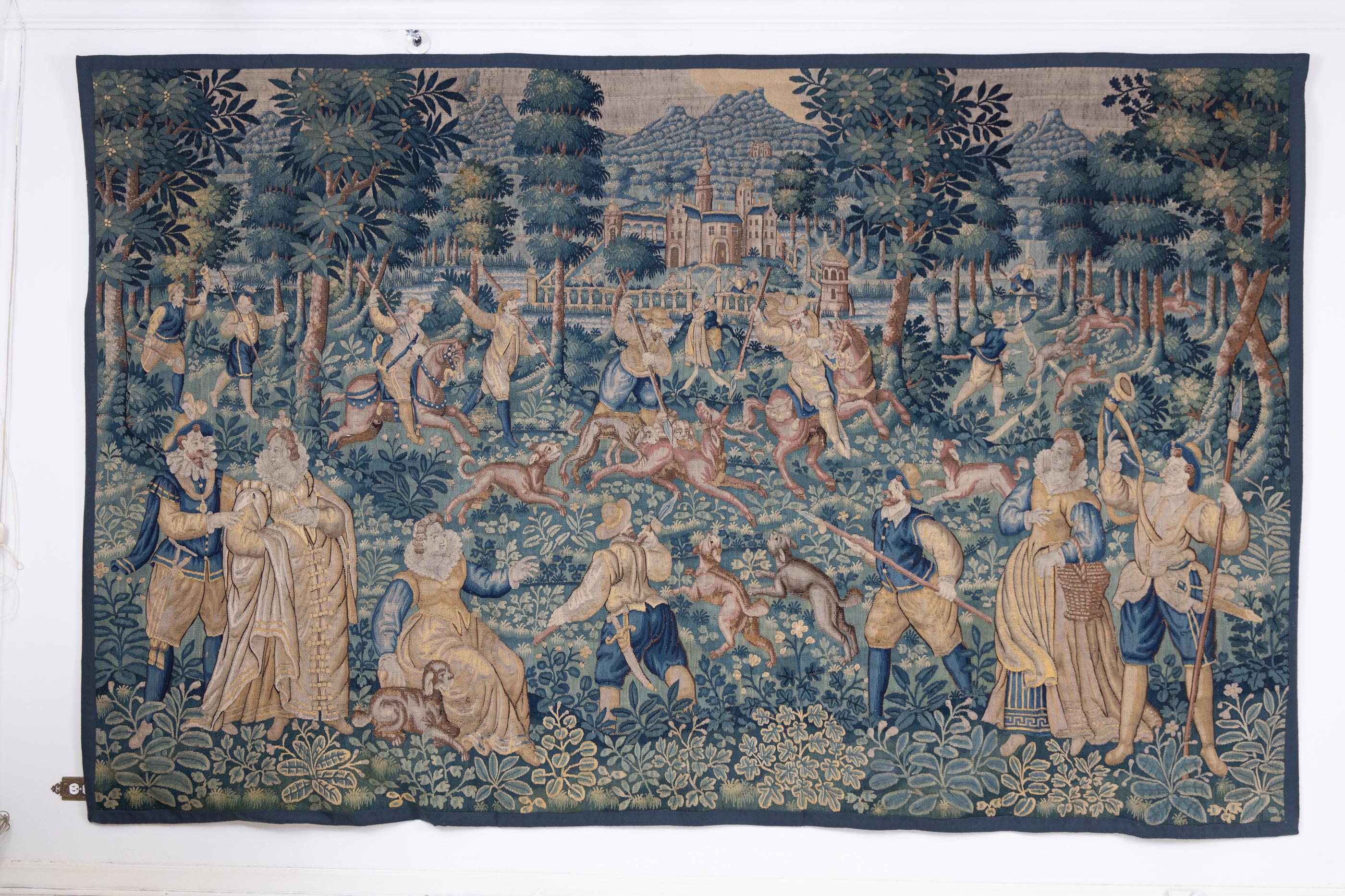 17th century French Elaborately loomed large tapestry with mountains and castle in background, depicting flushers blowing their horns to flush deer from the forest; hunters on horseback and on foot with staffs, going after deer with long spears, and