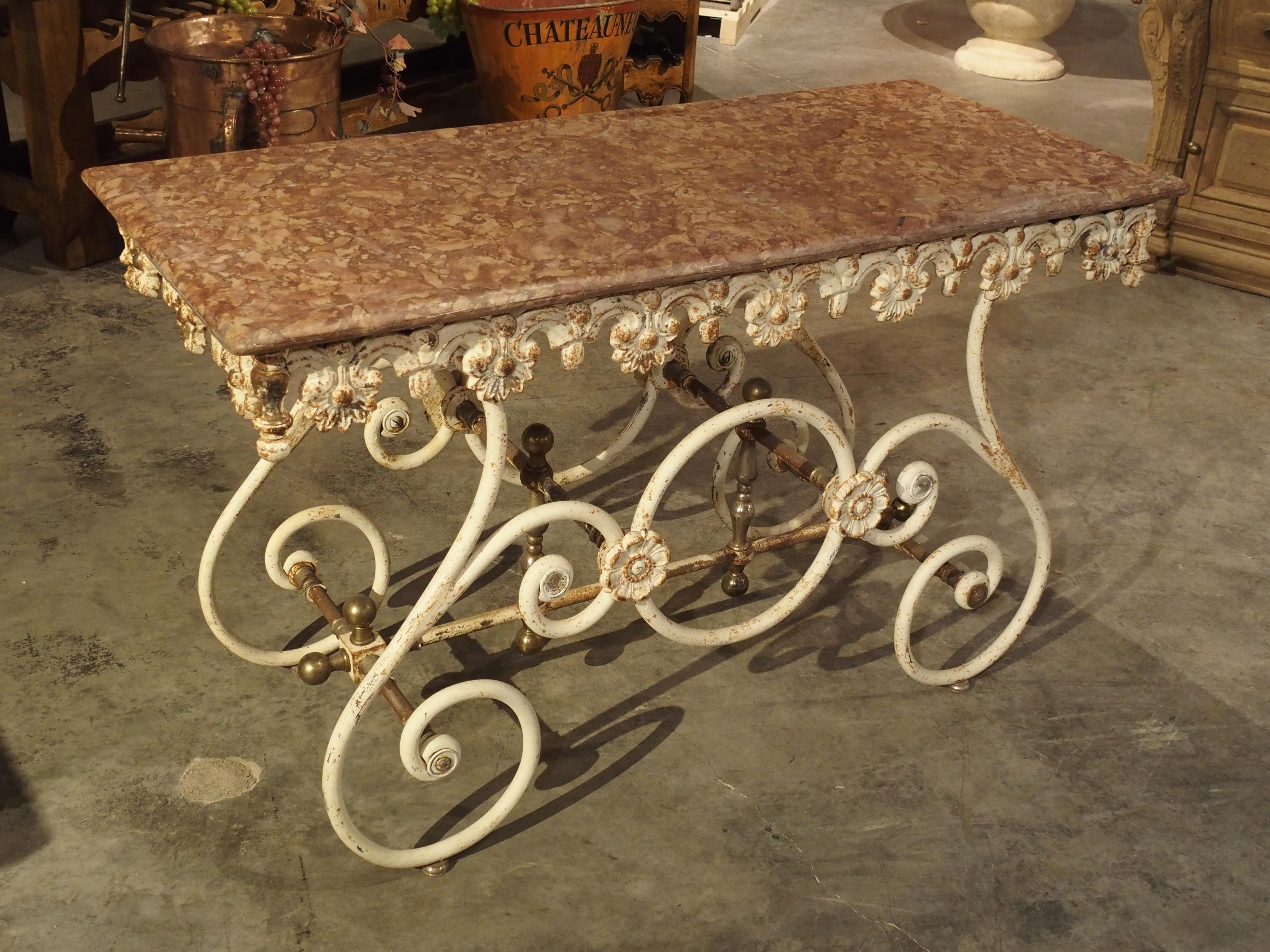 This is an unusual antique French pastry or butchers table in that it is quite shallow in depth, has a beautiful Rosso Verona marble, and has a base composed of large swooping C-Scroll wrought iron legs. Tables of this category are sometimes