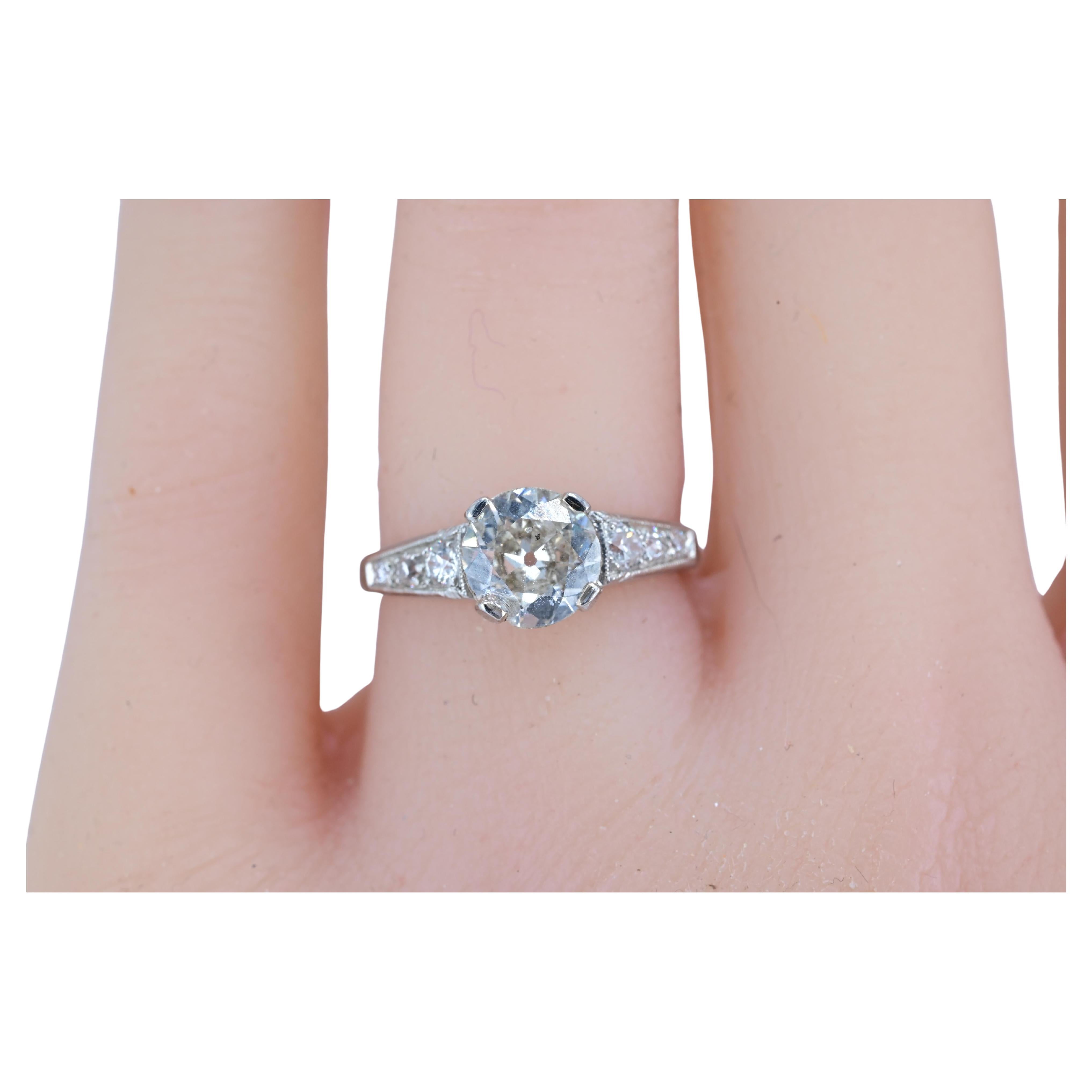 This is a classic antique or vintage diamond engagement ring, likely from the Art Deco or early 20th-century era, set in .900 platinum.

Design Features:
	•	Center Diamond: The ring features a round-cut diamond,  an Old European Cut or Circular