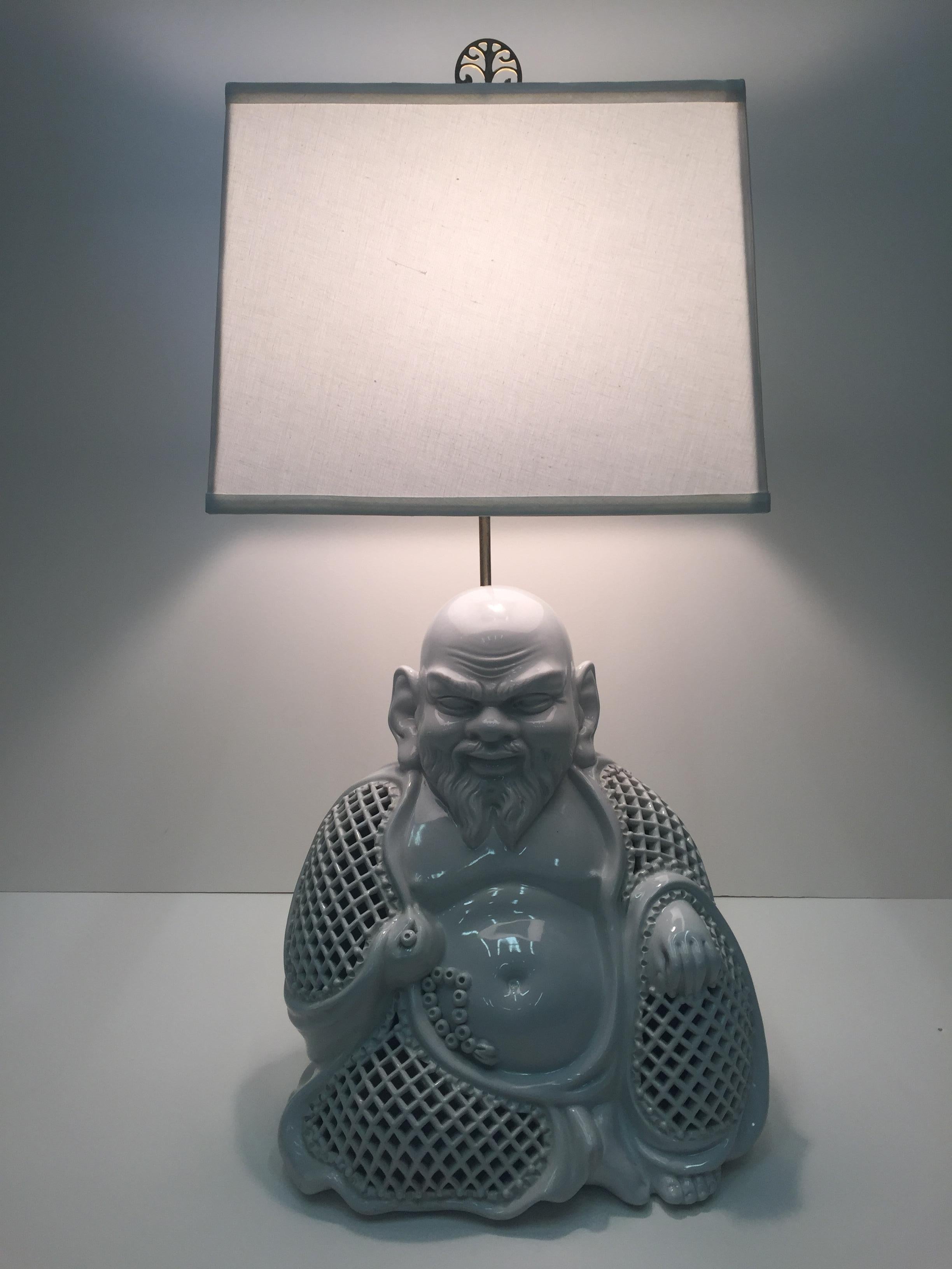 A sensational white ceramic table lamp having a sculptural Buddha with pierced body and happy expression and a beautiful Chinese decorative brass finial.
Shade not included, the one shown is 14 x 14 x 10.
