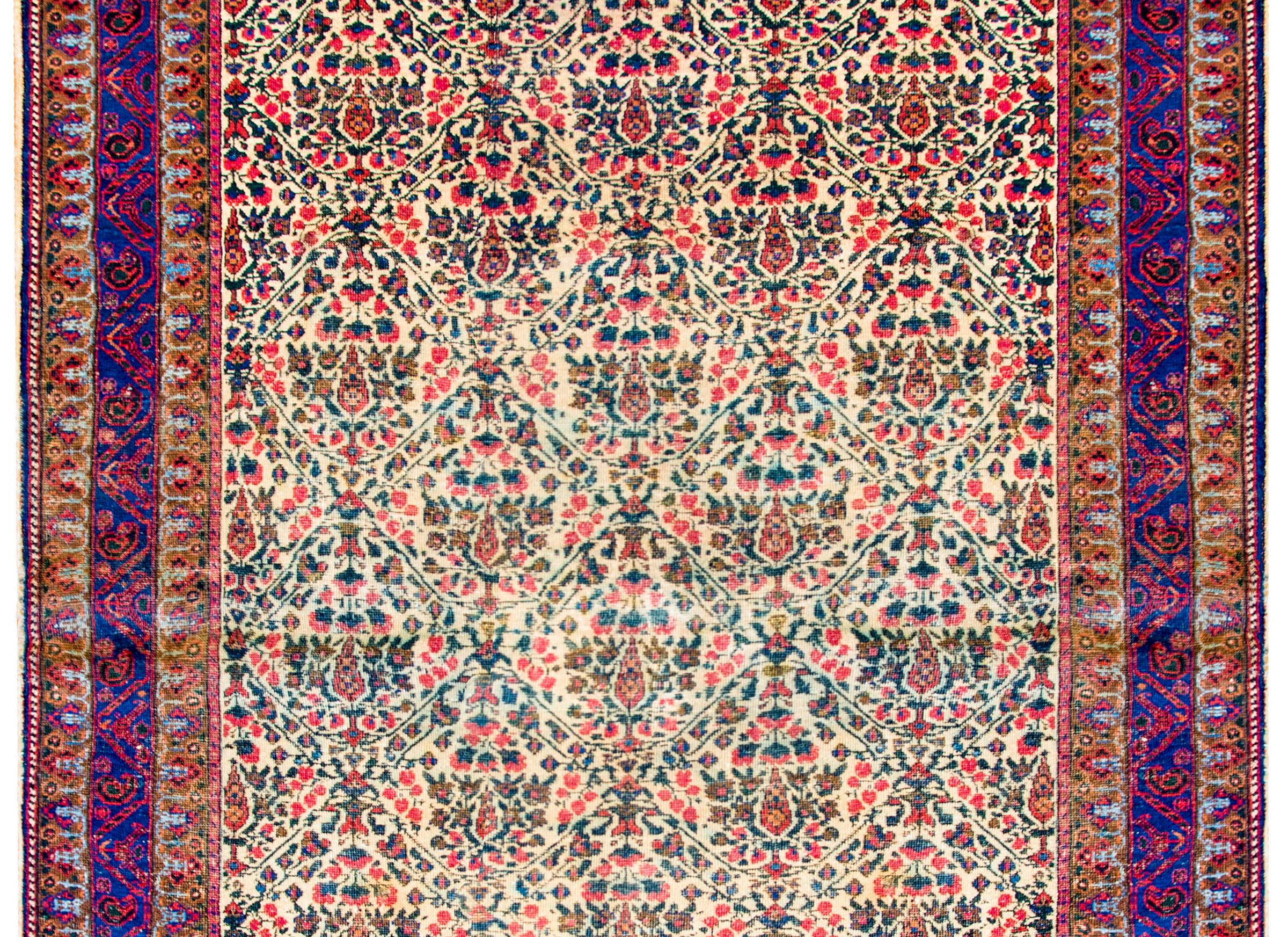 An early 20th century antique Persian Afshan rug with an all-over densely woven tree-of-life pattern woven in crimson, green, and indigo, on a cream colored background, surrounded by a wide border containing a large central stylized floral and vine