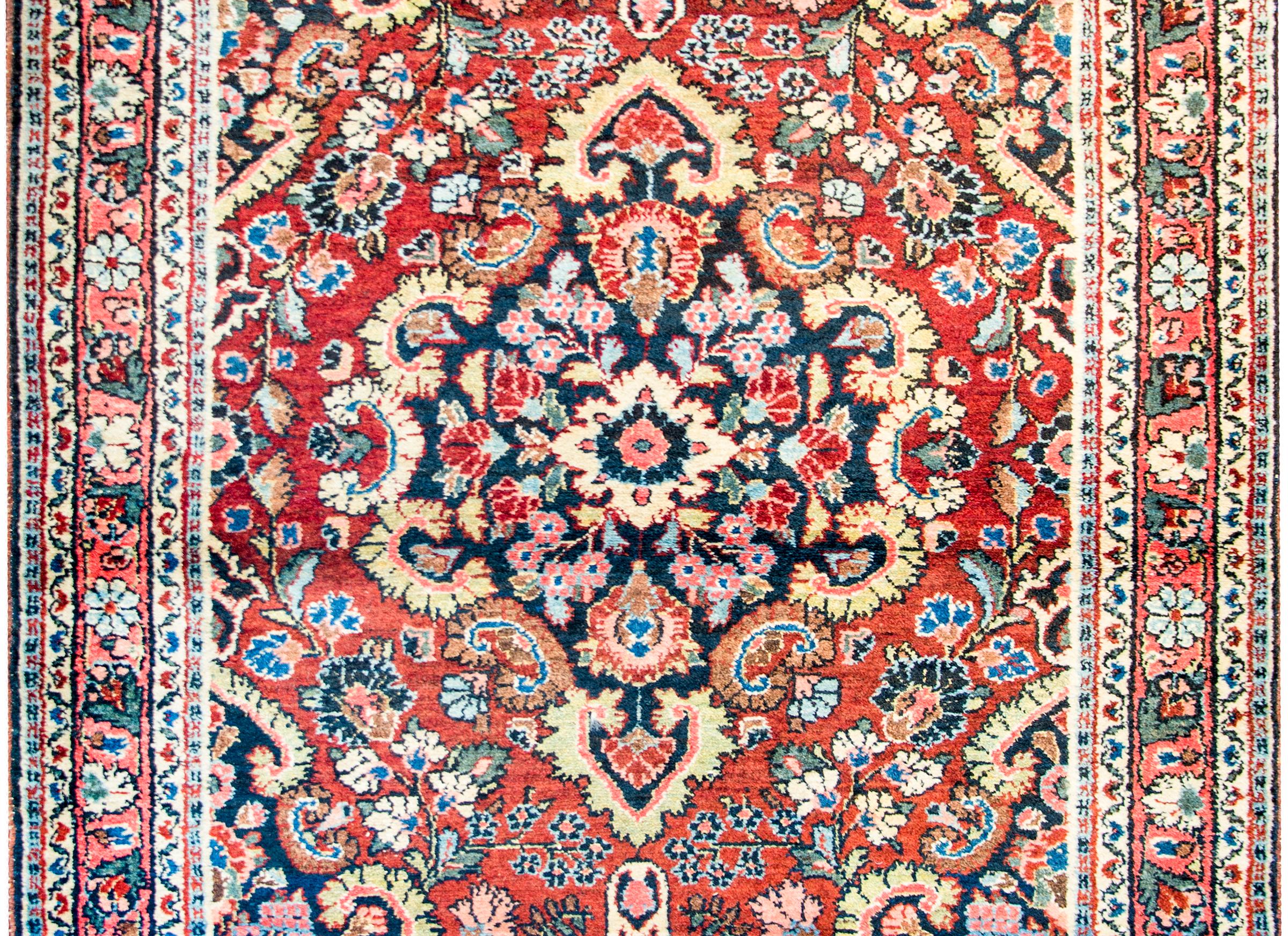 A fantastic early 20th century antique Persian Bibikibad rug with a large central floral medallion woven in bold crimson, pink, light and dark indigo, and cream colored wool on a dark indigo background. The medallion lives amidst a field of densely