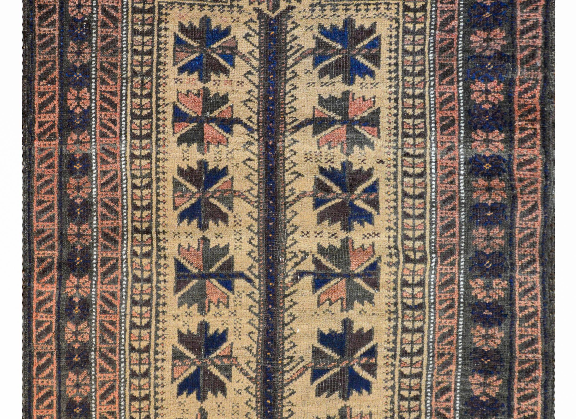 A fantastic early 20th century Persian Baluch prayer rug with a large-scale stylized floral pattern woven in brown, indigo, and pale red on a cream colored background. The border is composed with multiple geometric patterned stripes woven in similar