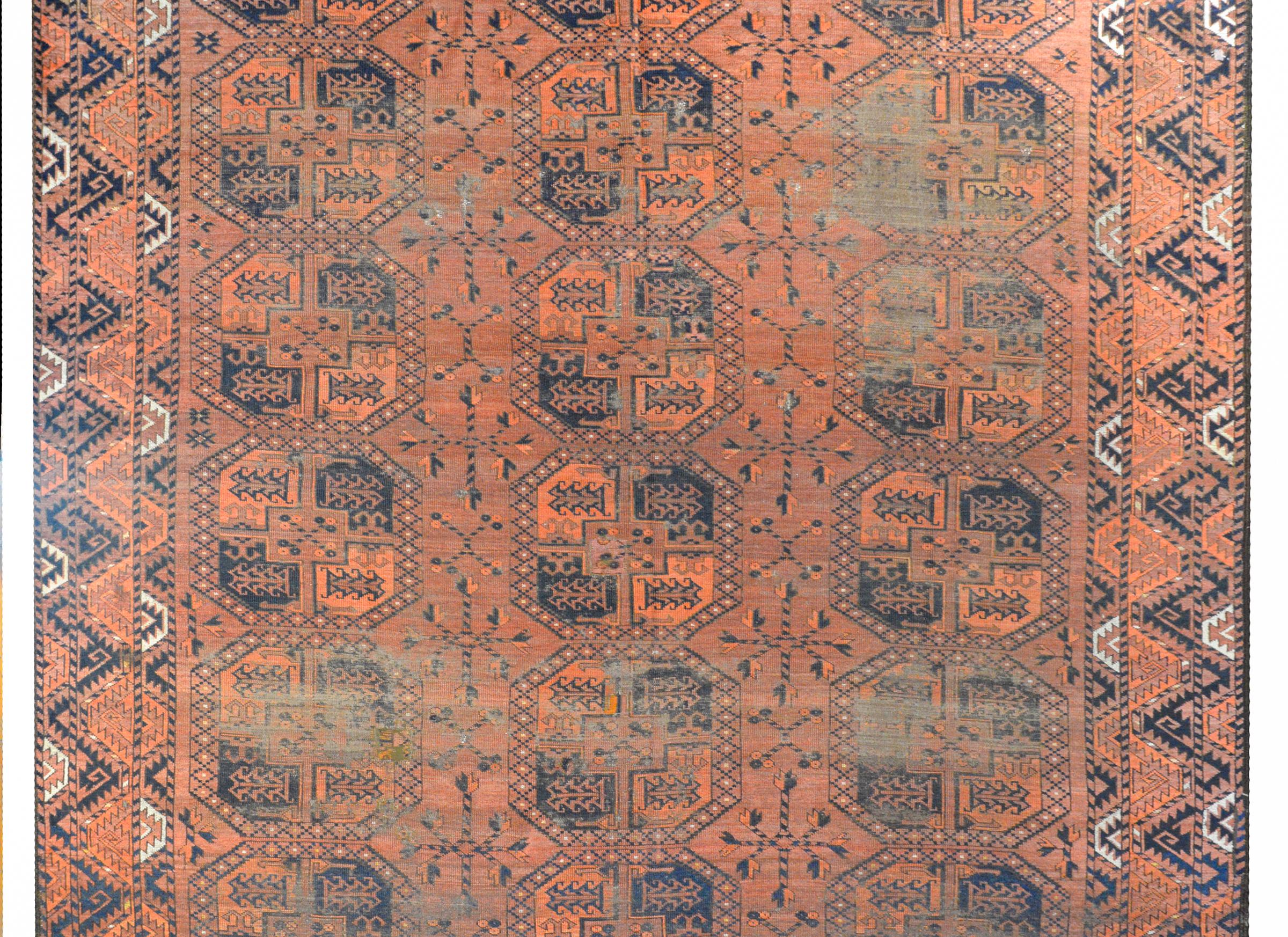A fantastic early 20th century Afghani Ersari rug with multiple all-over crimson and indigo octagonal medallions amidst a field of stylized flowers and scrolling vines all woven in crimson and indigo on a pale crimson background. The border is