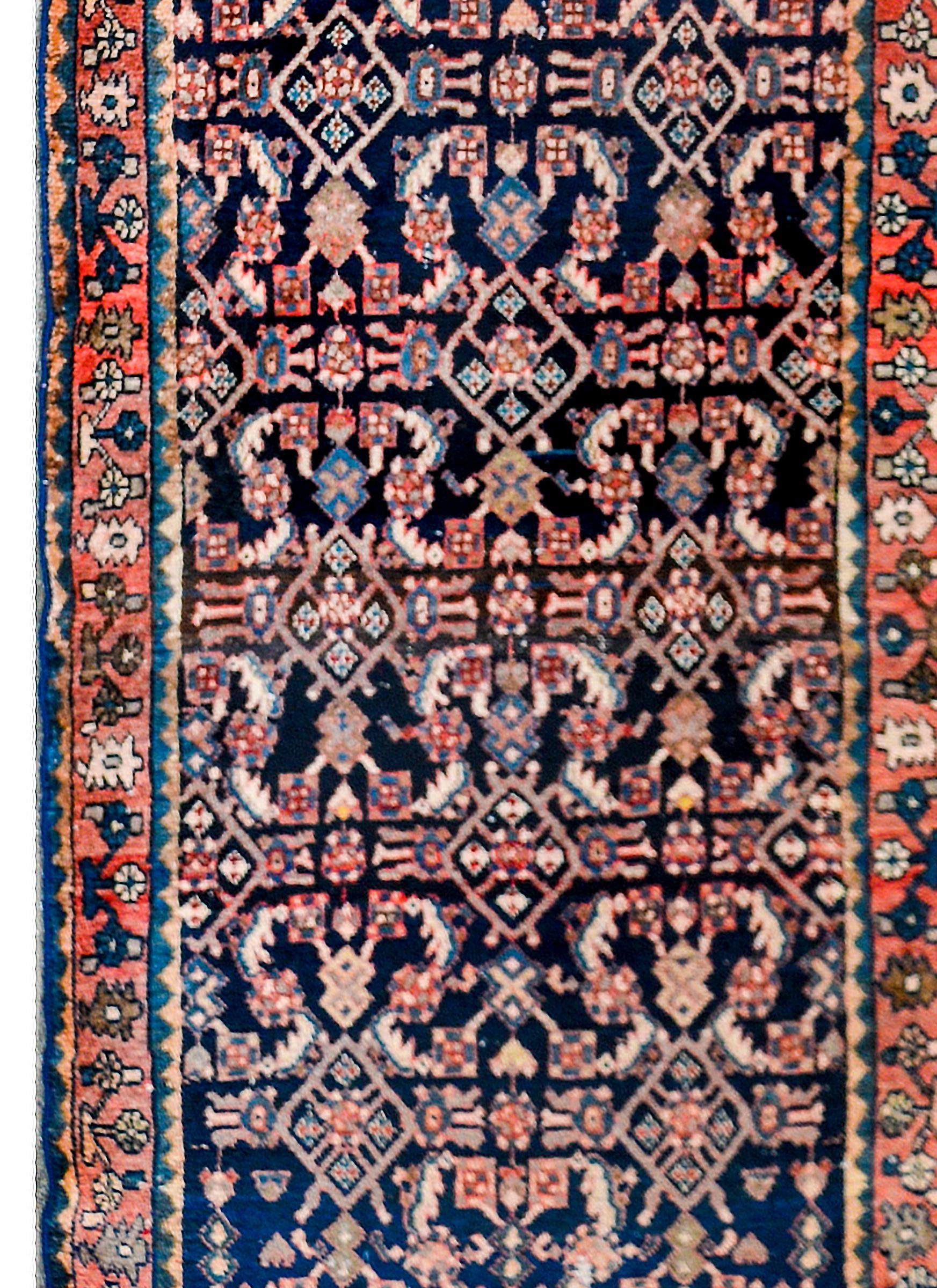 A fantastic early-20th century Persian Hamadan rug with an all-over mirrored trellis pattern of flowers and vines, woven in crimson, pink, light indigo, and white colored wool, on a dark indigo background. The border is complex with a large-scale