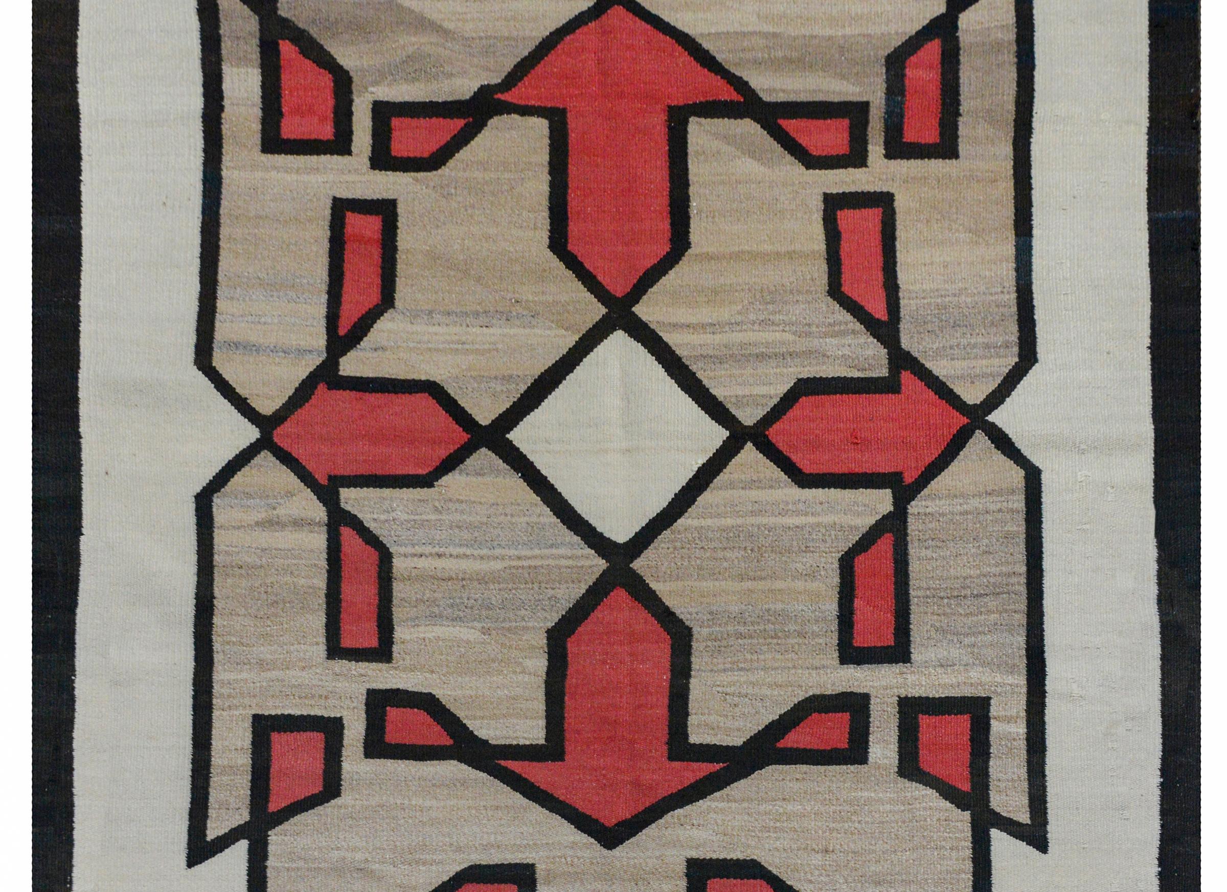 A fantastic early 20th century Navajo rug with four large red arrows pointing outward from a central white diamond, amidst a field of other geometric shapes on an abrash natural gray wool background.