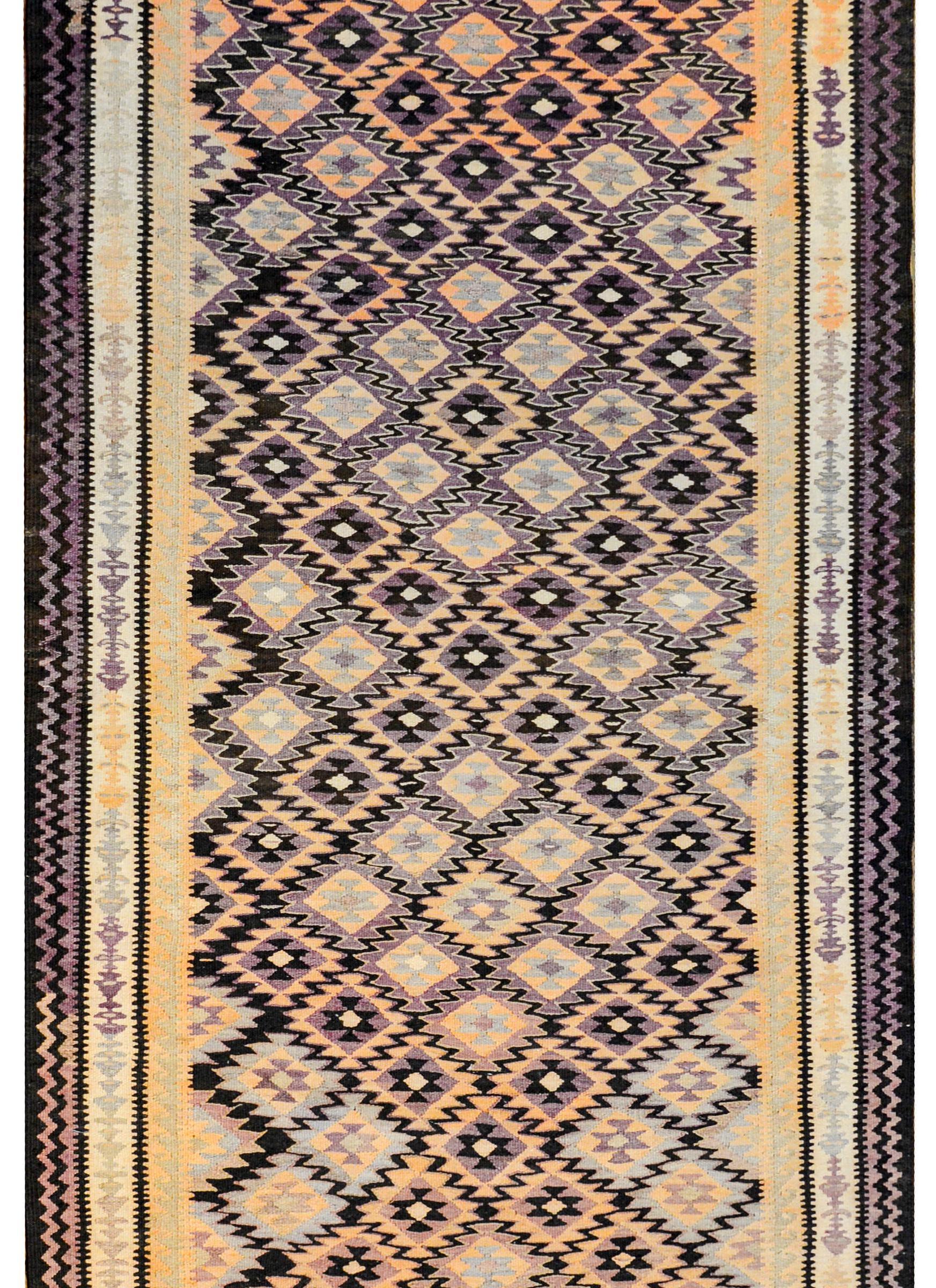 A fantastic early 20th century Persian Qazvin kilim runner with a wonderful geometric pattern of multi-pointed stylized flowers woven in orange, lilac, grey, and black colored wool arranged in a way that a zigzag pattern is created across the field.
