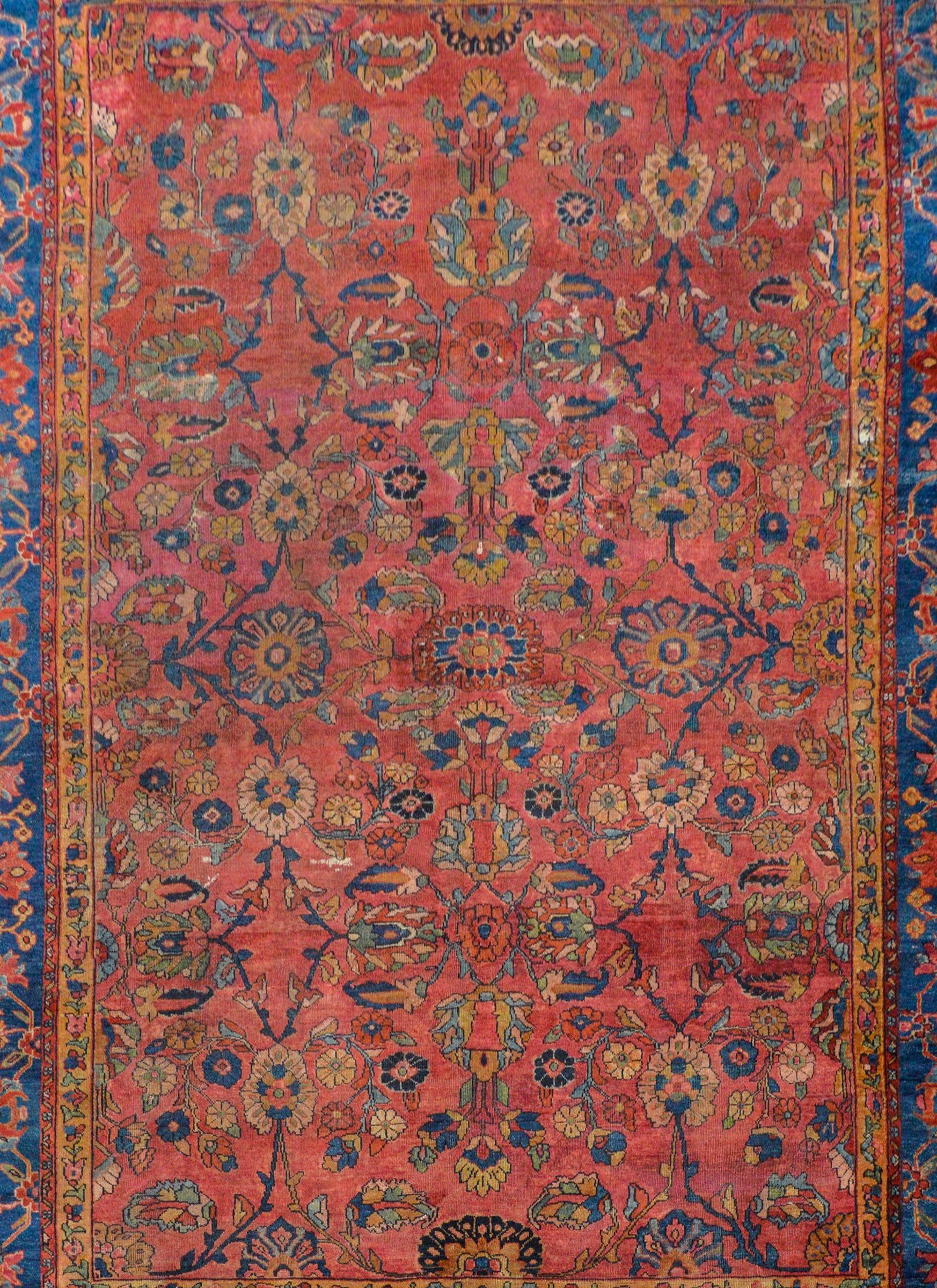 A fantastic early 20th century Persian Sarouk Mahal rug with an all-over field of flowers and vines woven in light and dark indigo, pale green, cranberry, and gold on a cranberry background surrounded by a wonderful border woven with large-scale