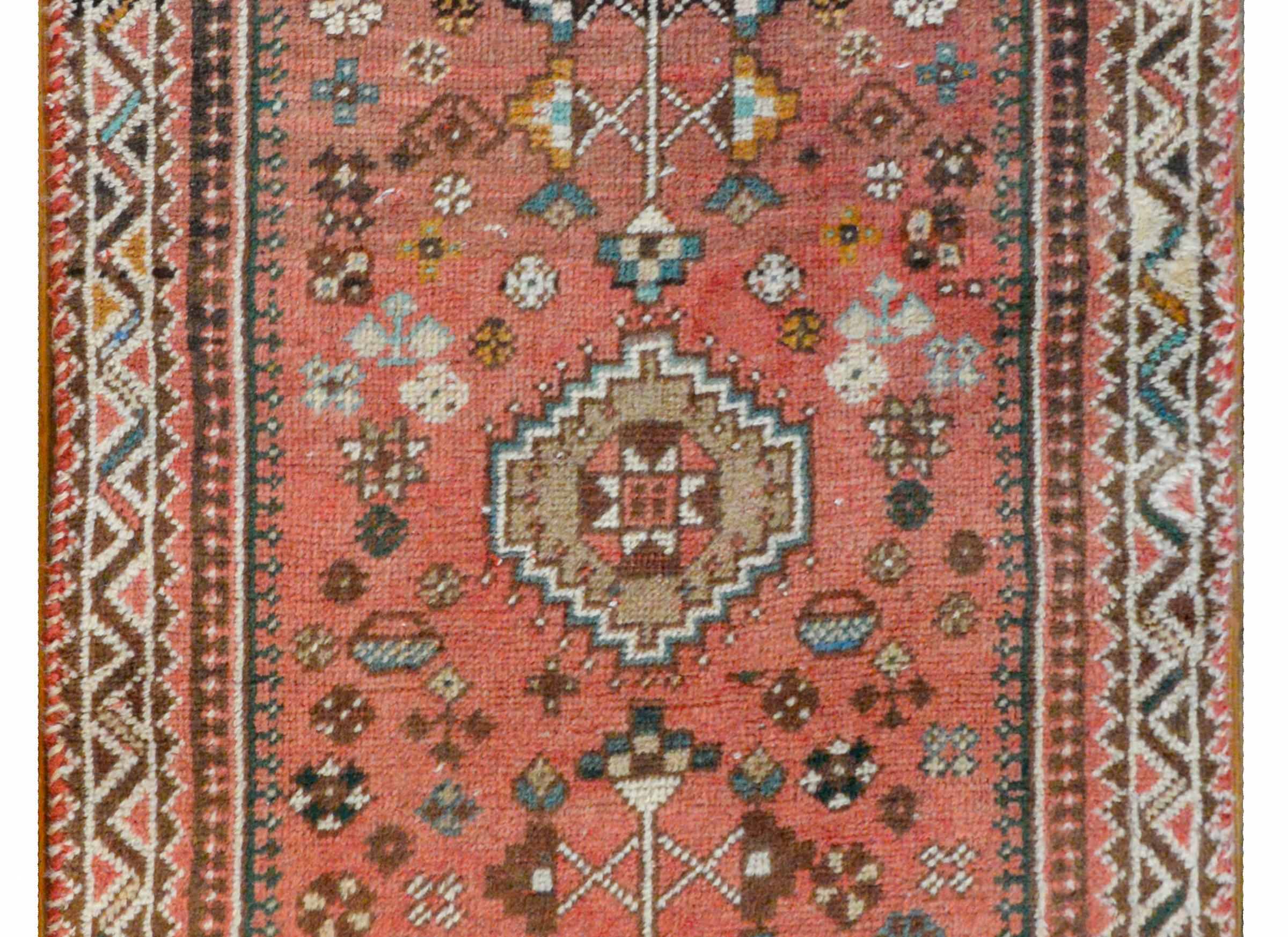 A fantastic early 20th century Persian Shiraz runner with a bold tribally woven pattern containing a marlge stepped diamond medallion amidst a field of stylized geometric flowers all woven in indigo, cream, yellow, brown, and indigo colored