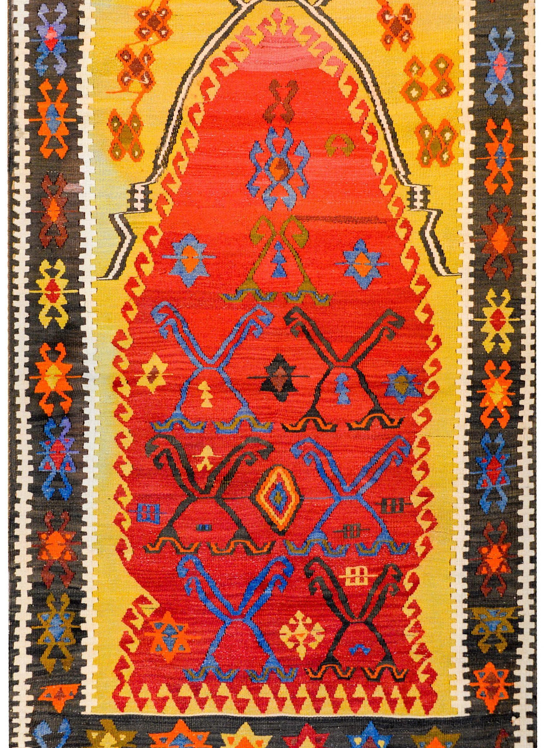 Un fantastique tapis de prière Kilim turc du début du 20e siècle avec un incroyable et audacieux motif coloré de fleurs stylisées et de vignes tissées en indigo, vert et orange, sur un riche fond cramoisi entouré d'un cadre doré brillant avec des