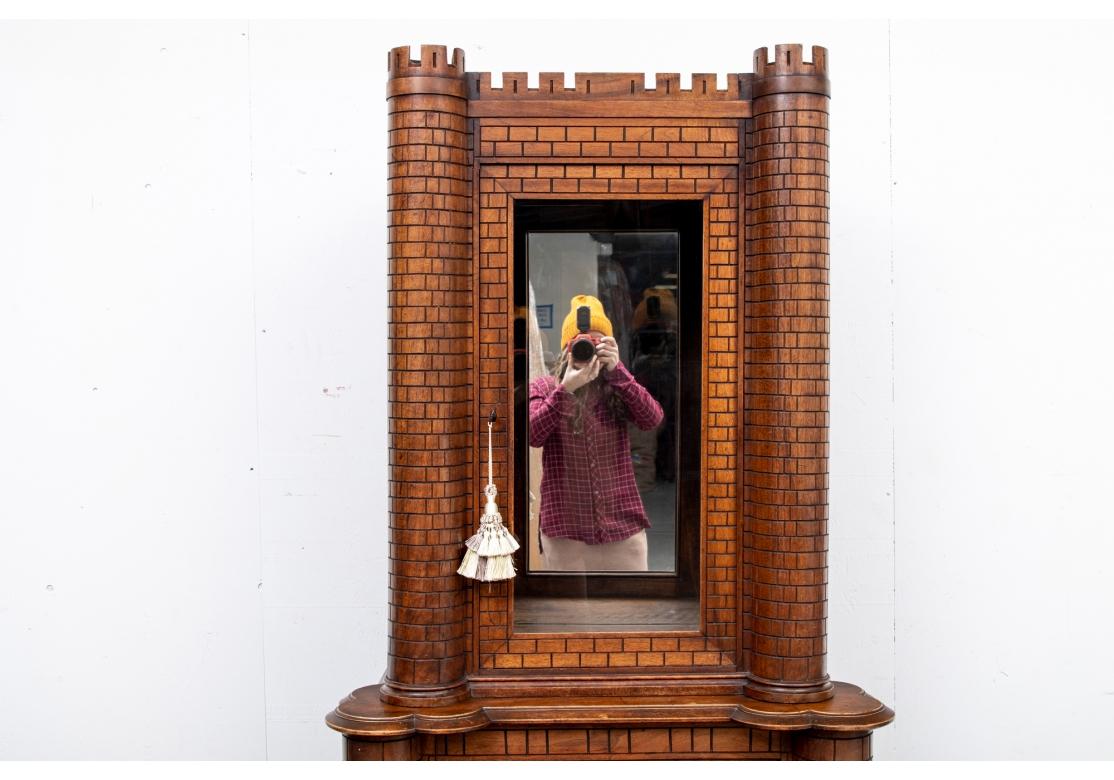 Originally purchased from the eponymous West Hollywood design shop Hollyhock. A two part cabinet in a carved castle form with overall linear brick pattern. The castle with twin turrets on trefoil shaped supports in the middle. With glass doors above