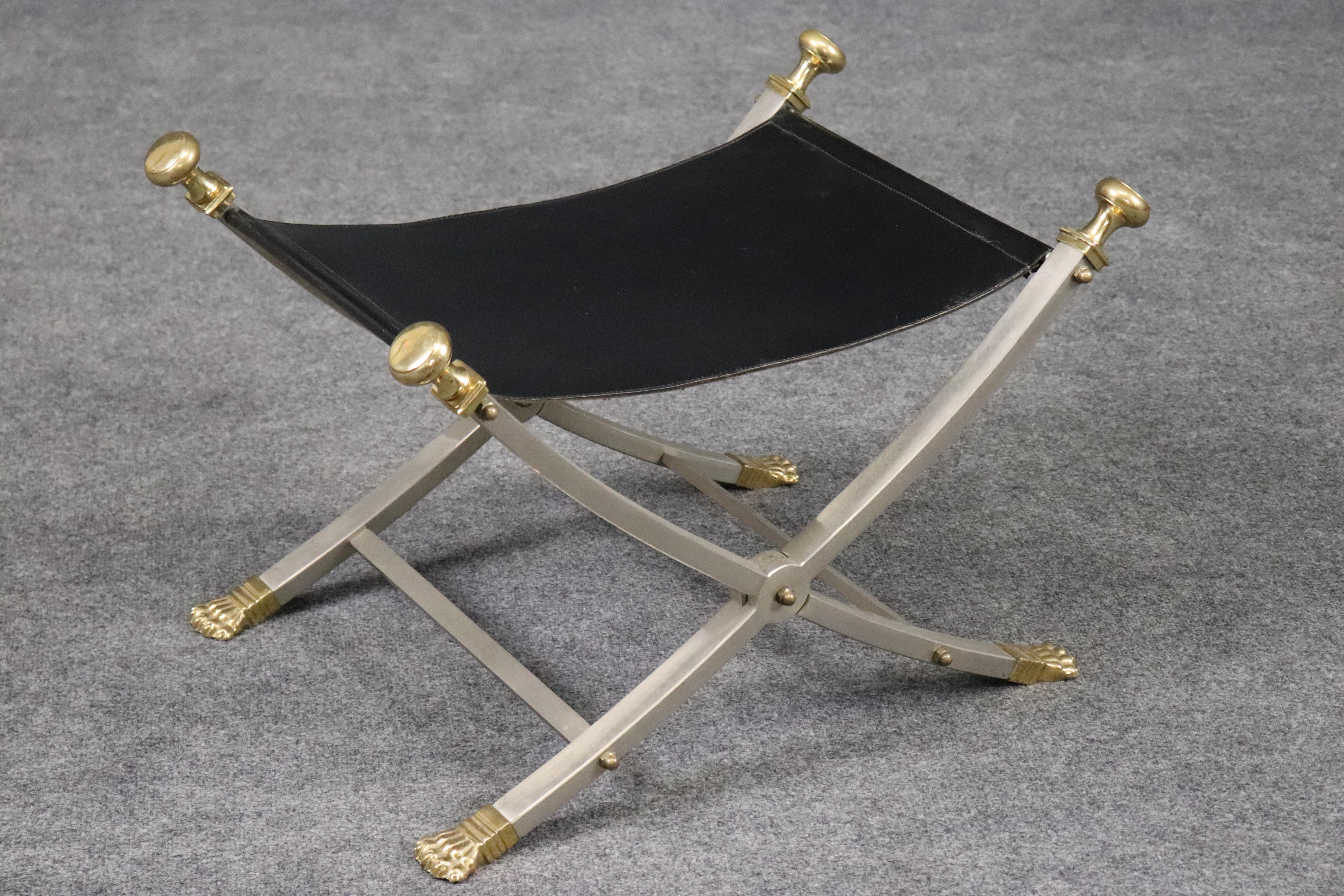 Se trata de un fantástico e icónico escabel plegable de campaña o de estilo Regencia de Maison Jansen. El taburete está en buen estado vintage usado. El asiento de cuero es plegable y el armazón es de acero y latón de gran belleza. El taburete data
