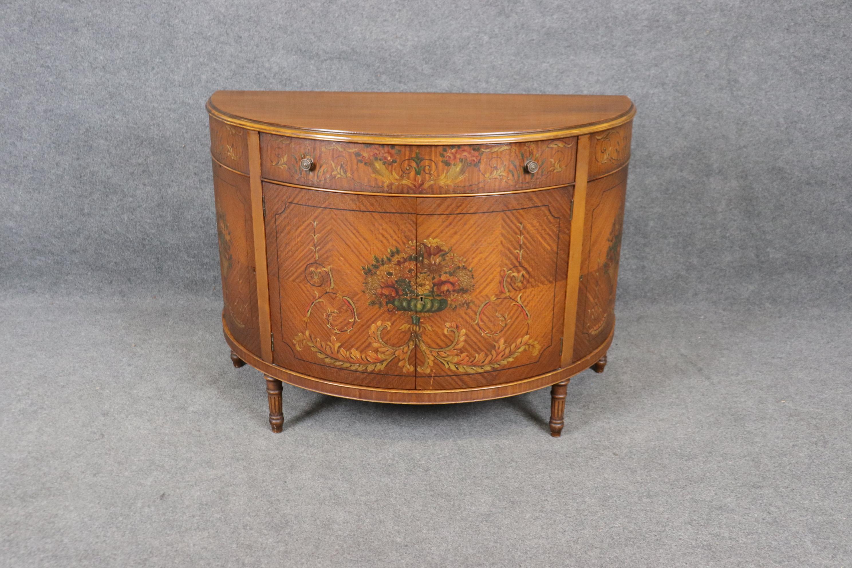 This is a spectacular Adams paint decorated commode in its original crackled finish with fantastic floral sprays painted throught the case. The demilune shape of the commode makes it perfect for use in a dining room as a buffet or server or an