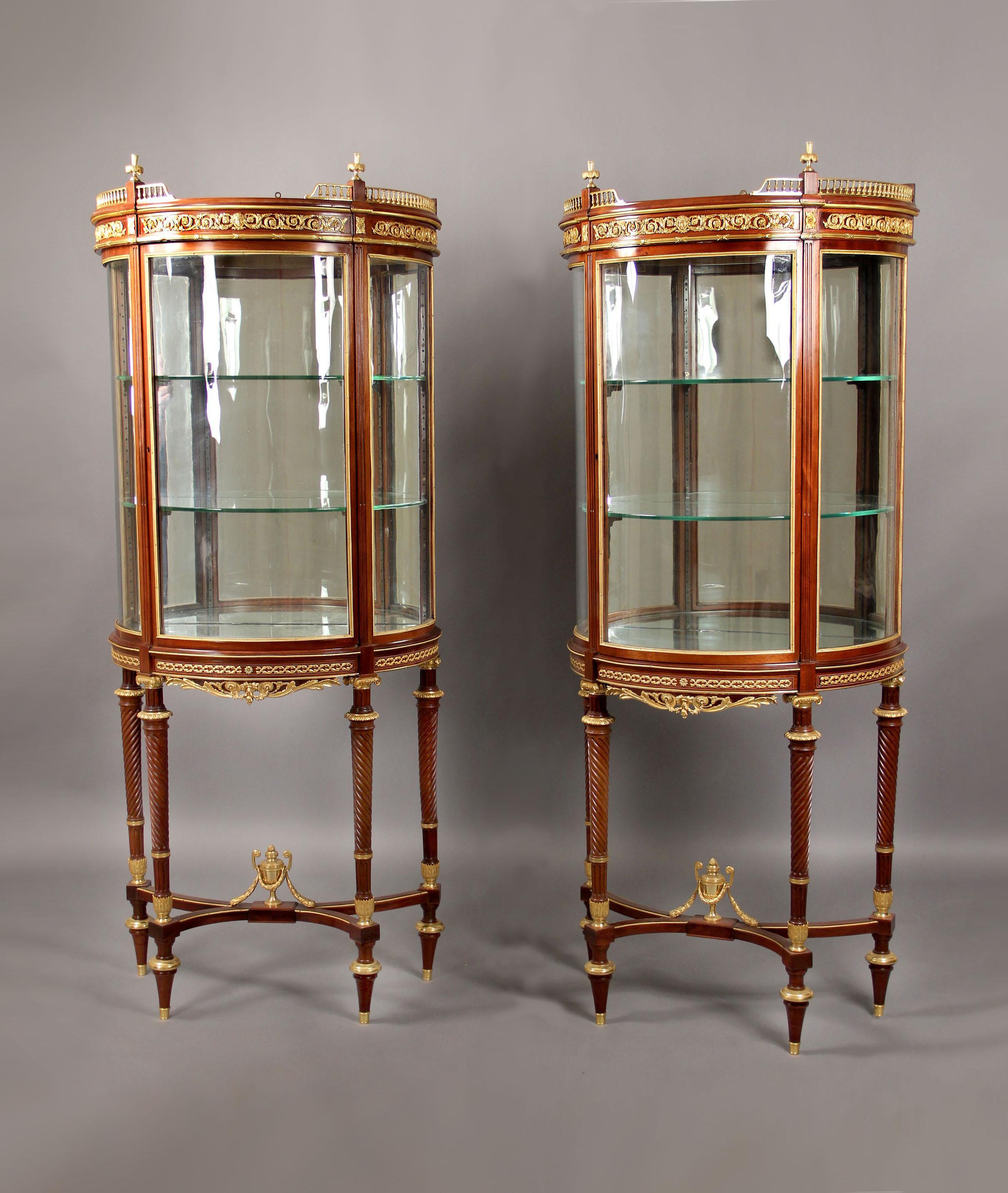 A fantastic pair of late 19th century Louis XVI style gilt bronze mounted demilune vitrine.

By Paul Sormani.

Each with balustrade galleries and raised on spiral decorated legs joined by a stretcher centered by a bronze urn.

Both vitrines