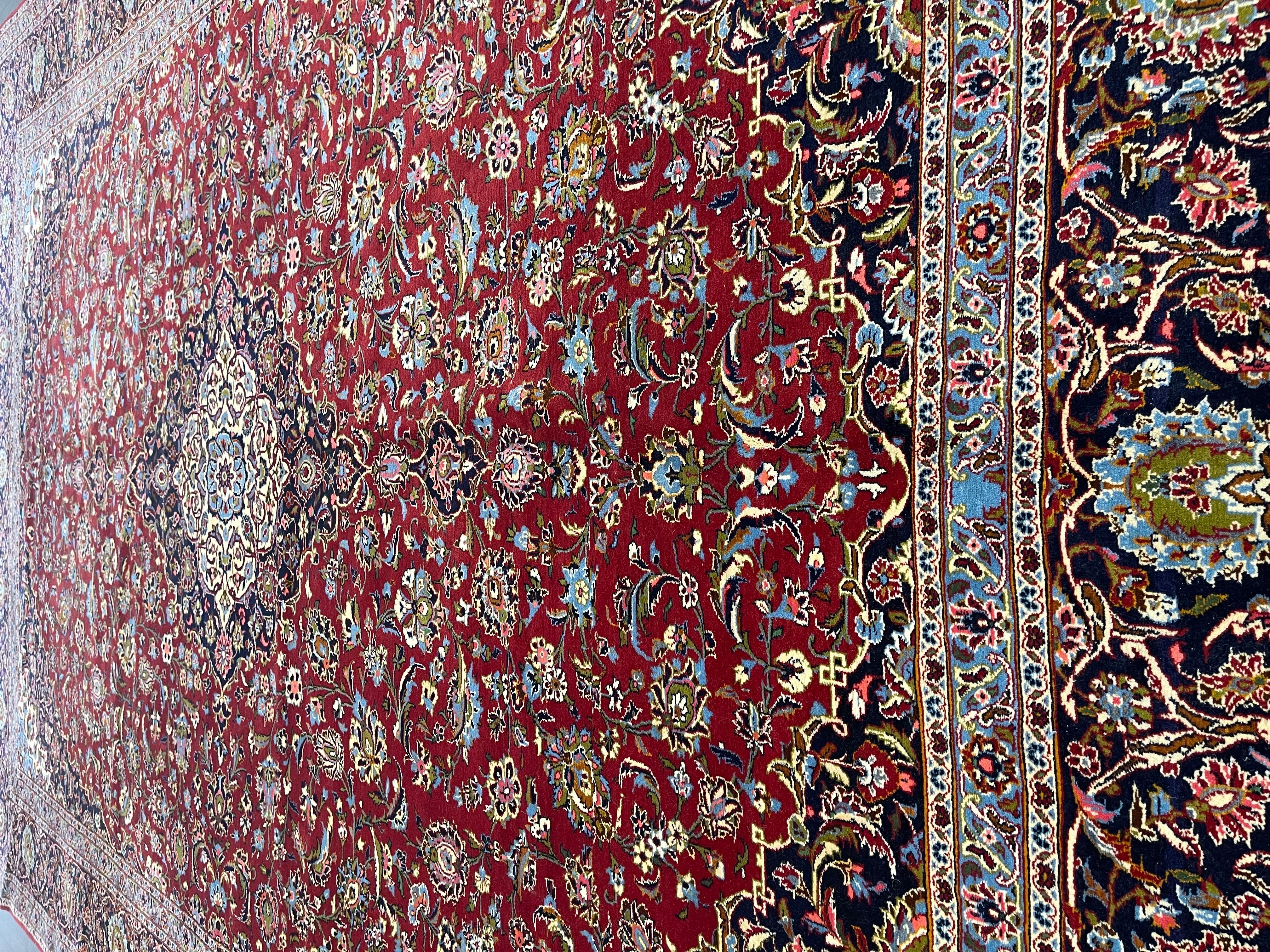 Ein klassischer Perserteppich, handgeknüpft von geschickten Knüpfern in Kashan, einem bedeutenden Zentrum der Teppichherstellung im westlichen Iran. Mit einem tomatenroten Feld, das mit Blumen und Blättern um ein Medaillon in der Mitte in Marineblau