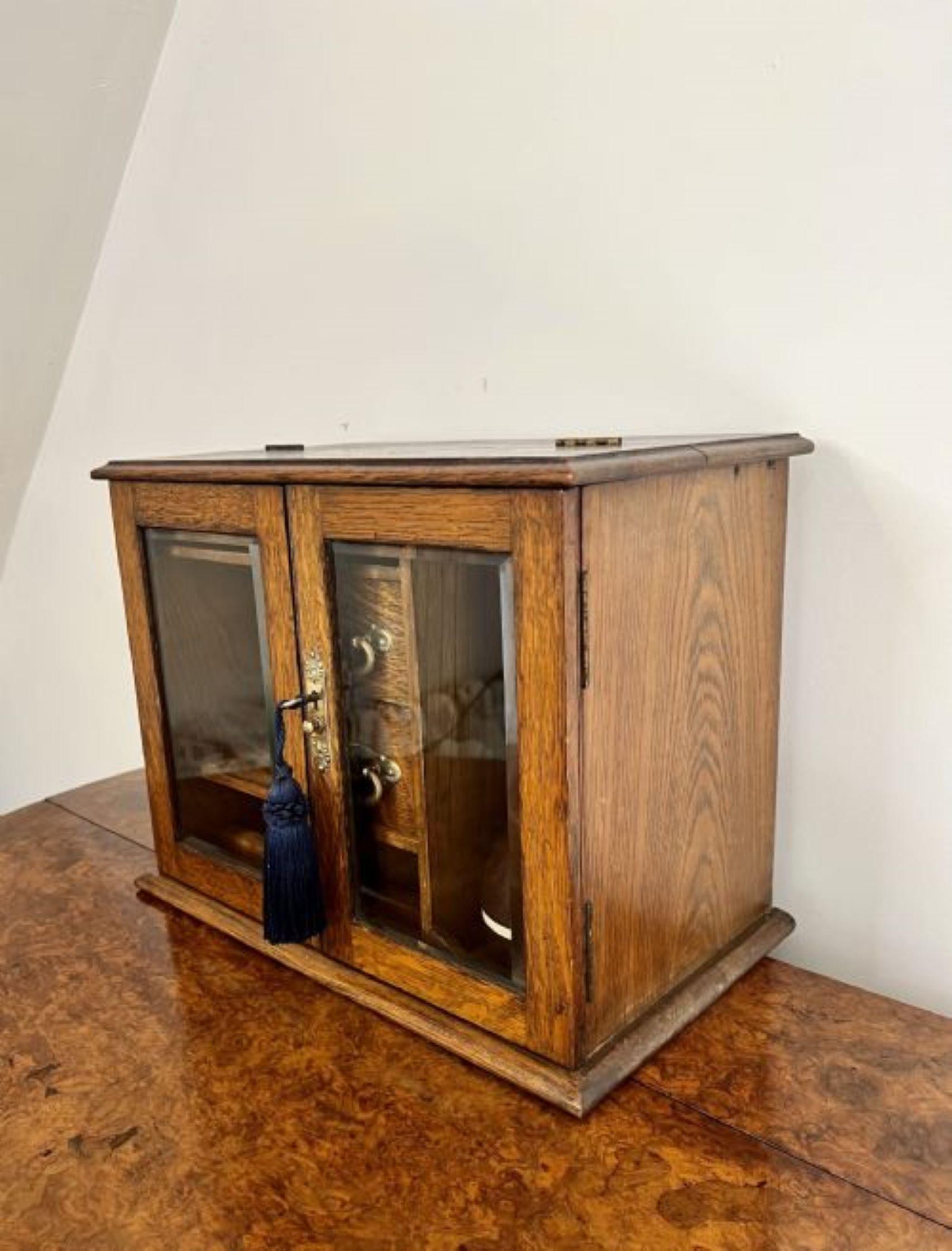 Fantastic quality antique Edwardian oak smokers cabinet having a fantastic quality oak smokers cabinet, with two glass doors to the front opening to reveal compartments for cigars, match boxes and smoking accessories with a pipe stand and two