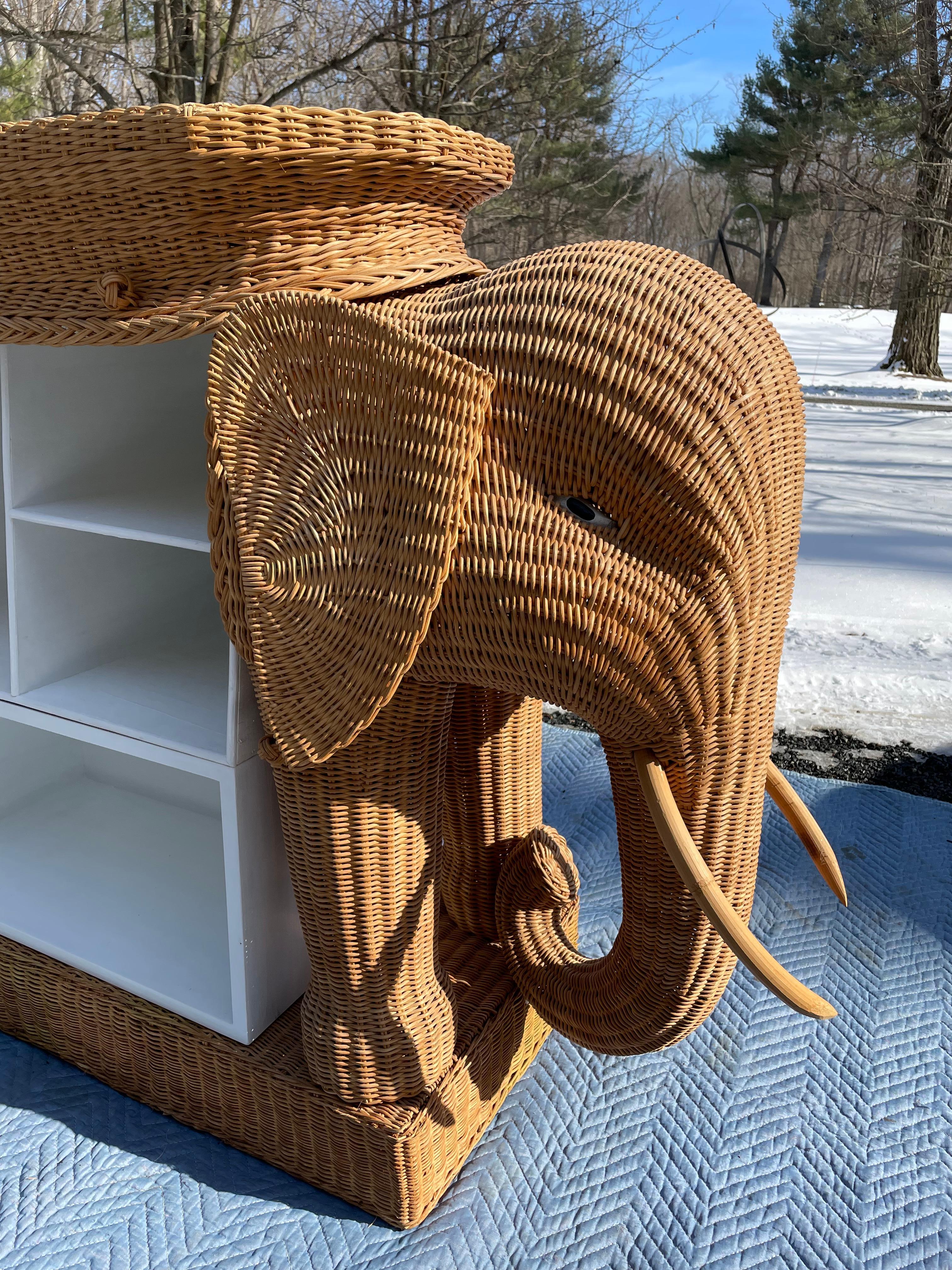 Fabulously whimsical vintage rattan dry bar having the form of two elephants facing in opposite directions. Each elephant is shown from head to shoulders with two front legs on a rectangular plinth. A long wooden oval top in white paint bordered in