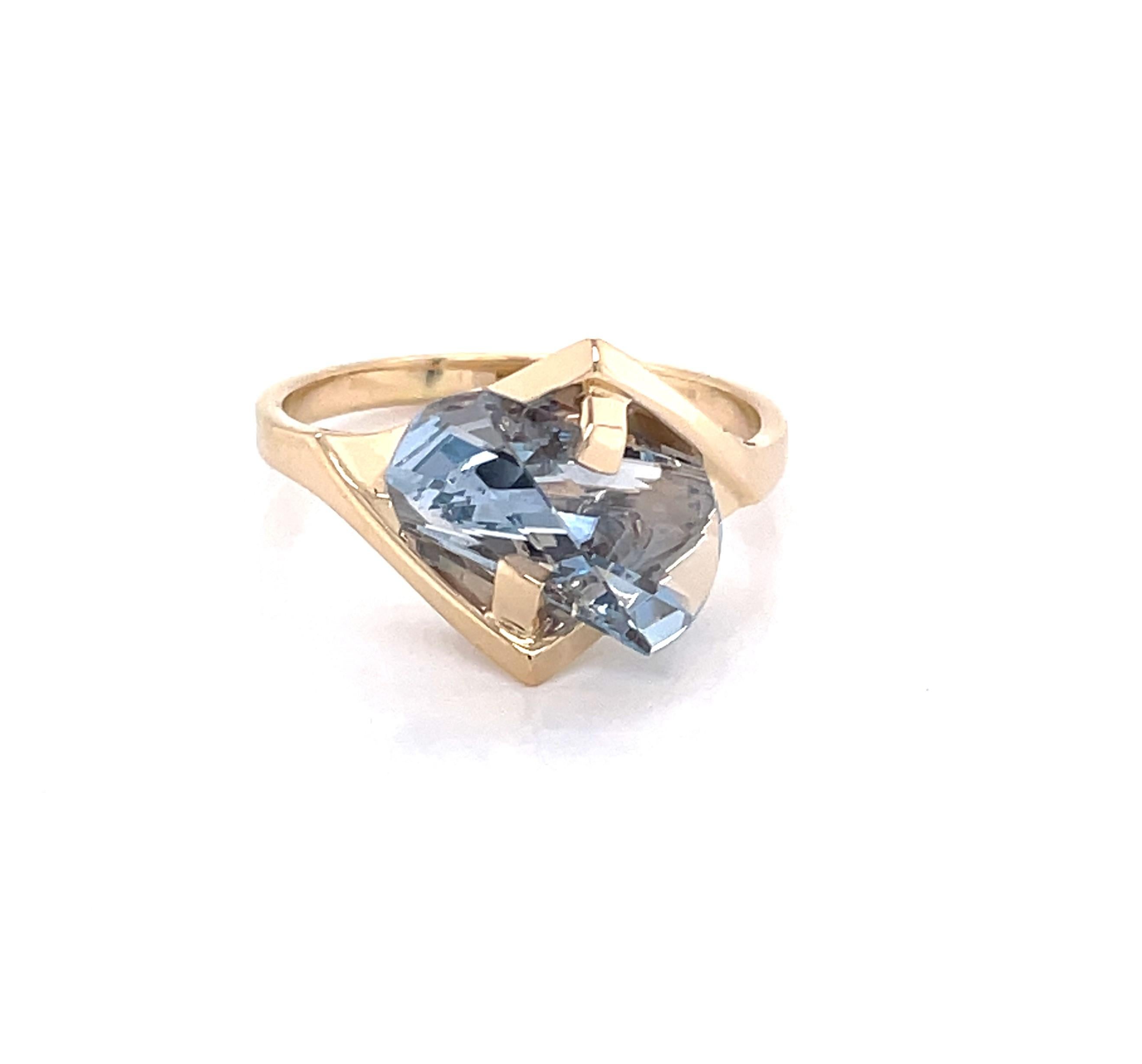 Appreciate this abstract shape stone and setting as a unique choice when looking for something special. The ice blue color and interesting fantasy cut of this topaz stone is stunning as it is suspended in the complementing fourteen karat 14K yellow