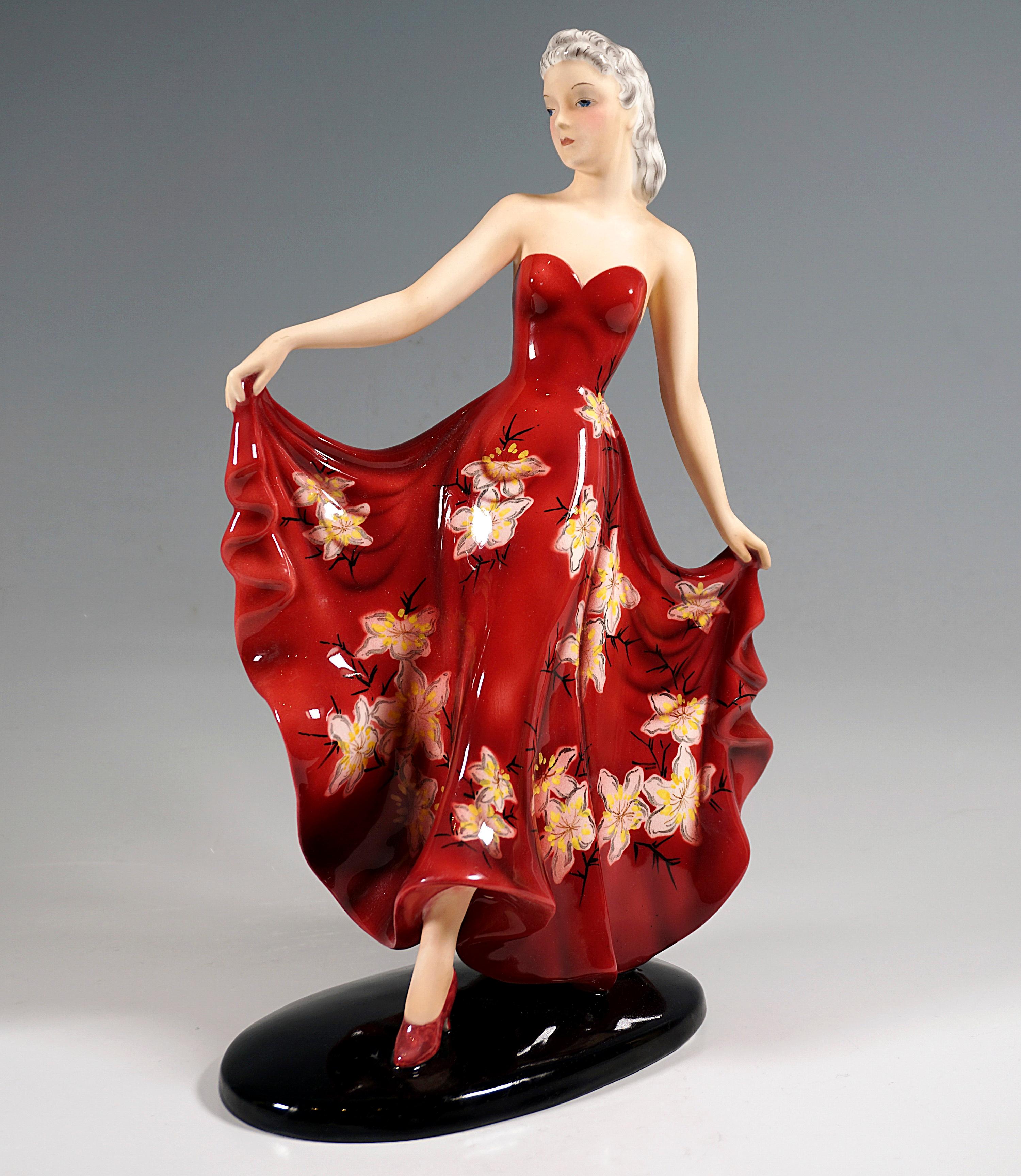Pretty young lady with her hair combed back, in a long, shoulder-free, red dress with floral decoration and high heels, elegantly striding along with her eyes slightly lowered, while holding up the hem of the skirt on both sides. Skin areas with a