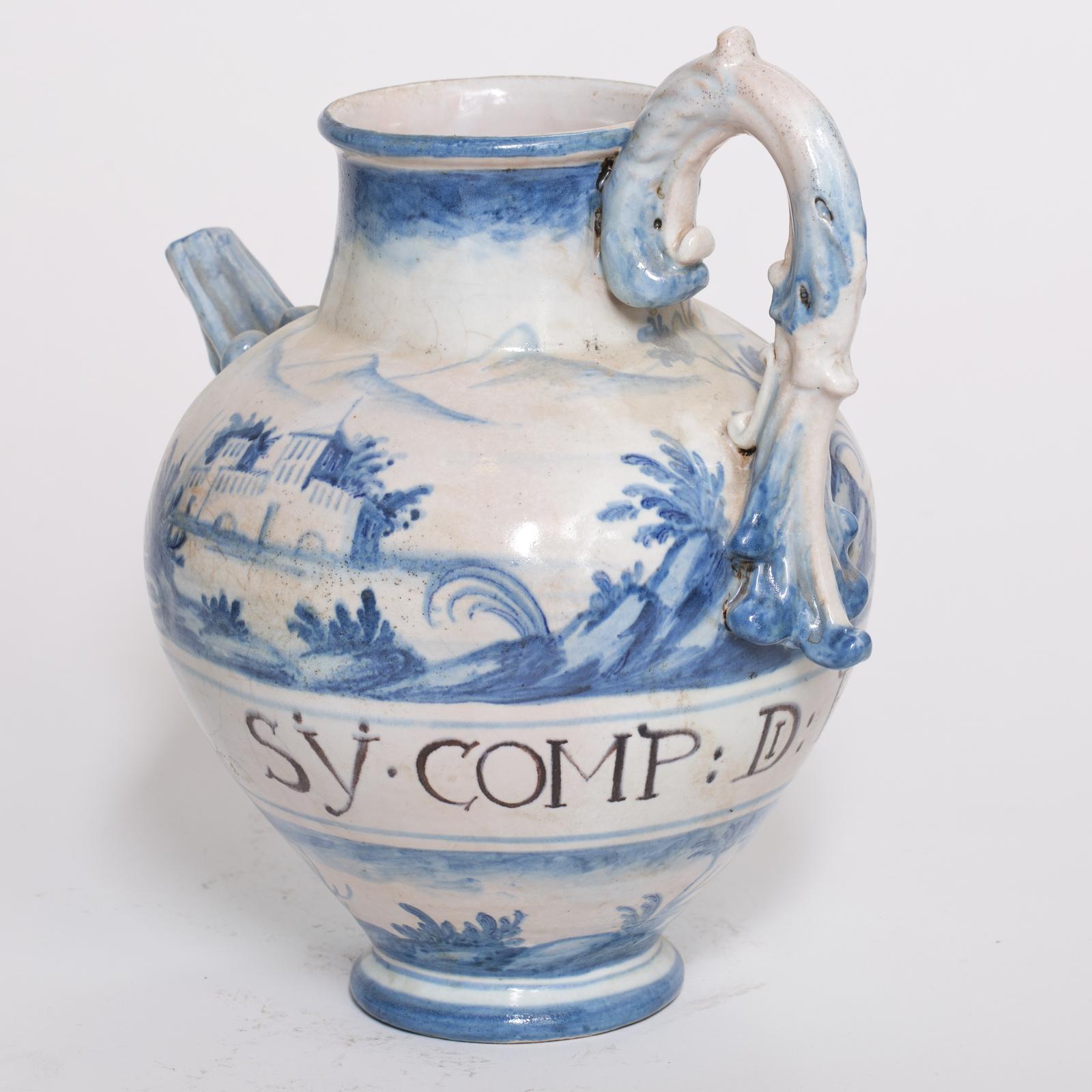 Masterful reproduction of an antique apothecary water jar with a spout and handle, entirely handcrafted by the maiolica artisans of Manetti e Masini in Florence. The jar is executed in the signature Ligurian maiolica style, namely motifs in white
