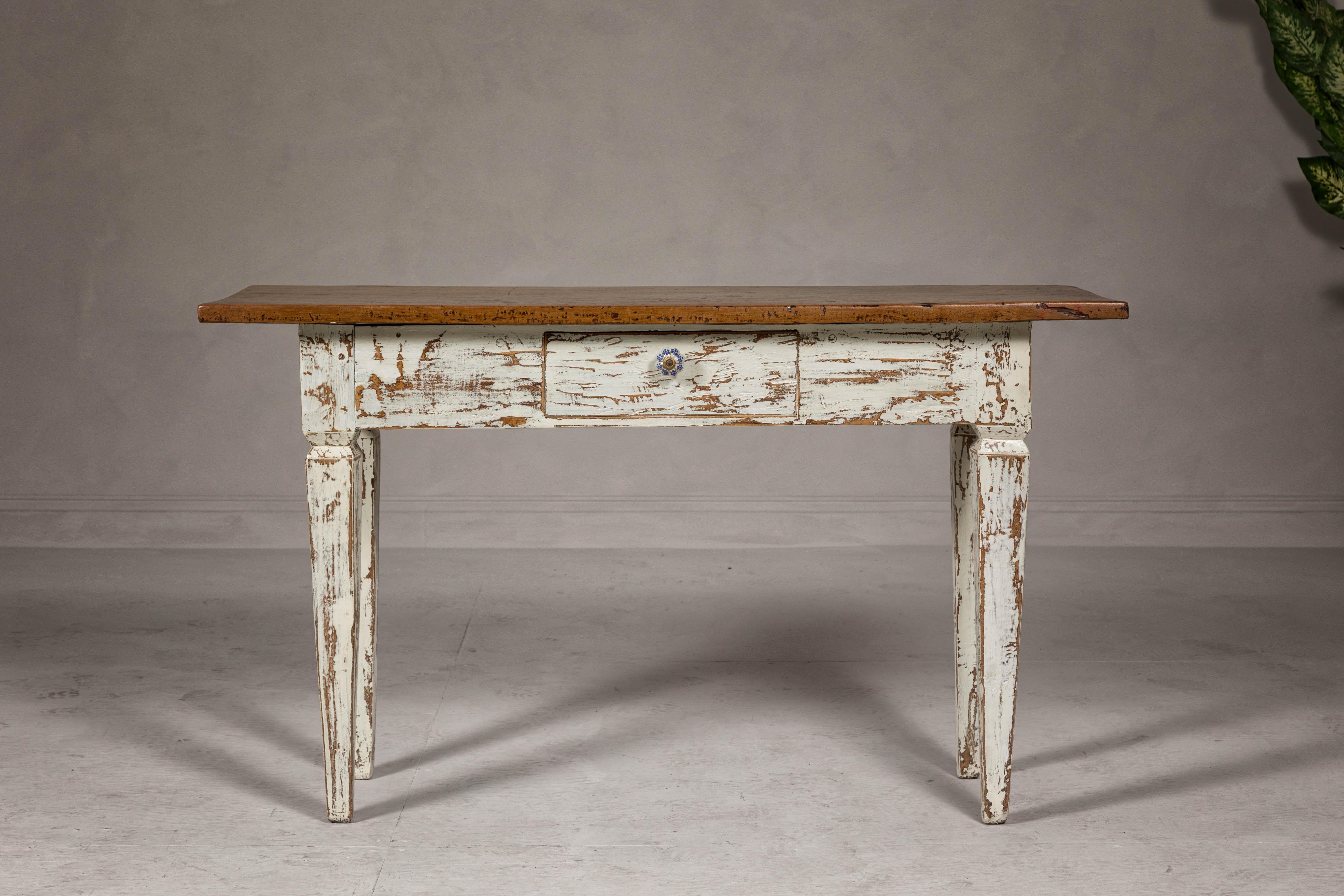 A Farmhouse chic country Neoclassical style sofa table with single drawer, distressed body and tapered legs. This farmhouse chic country Neoclassical style sofa table seamlessly blends rustic charm with elegant sophistication. A vintage piece that