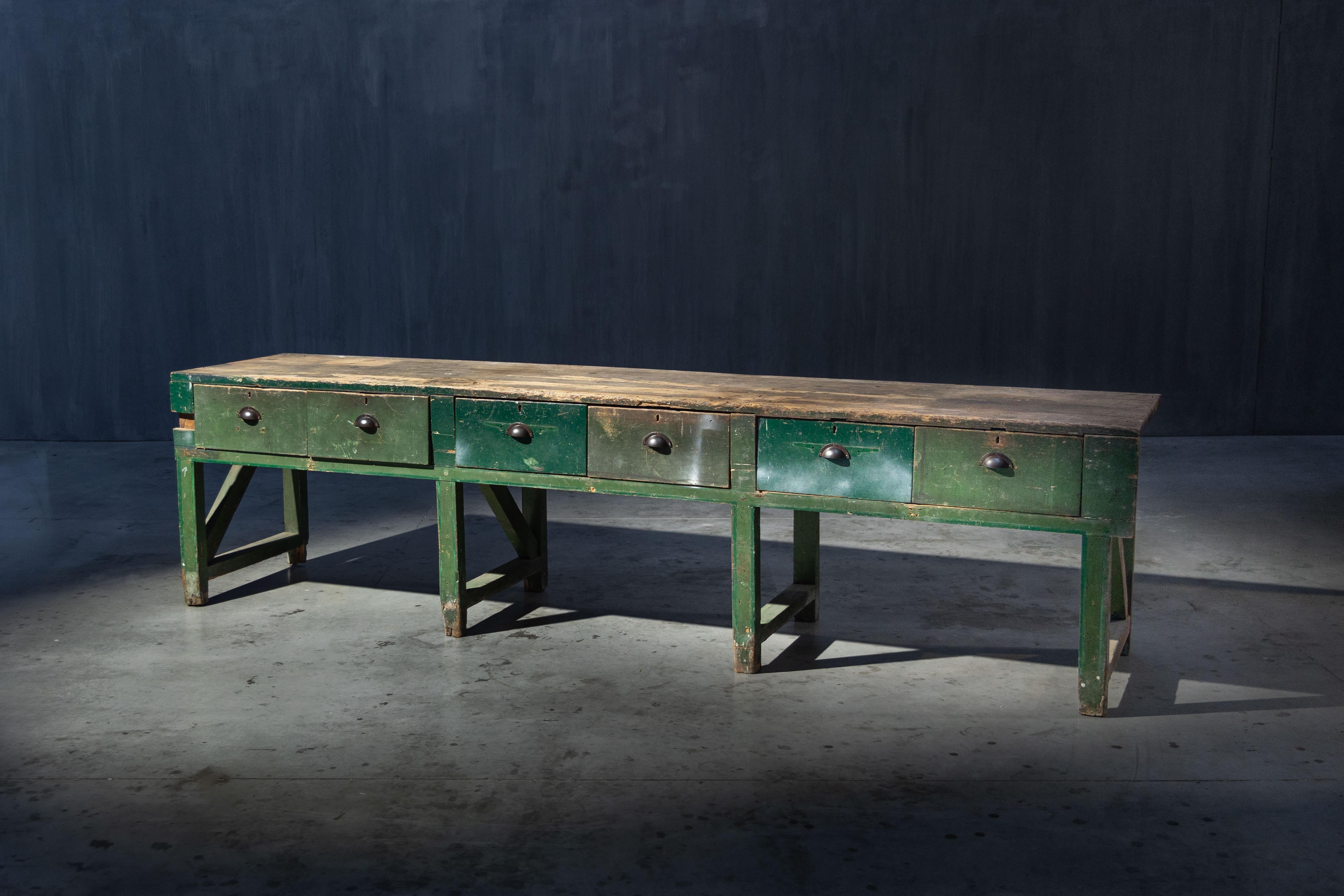 Cette table console de ferme de caractère date du début du 20e siècle et présente une charmante patine due à des années d'utilisation. Fabriqué en bois massif avec une base peinte en vert, il comprend cinq tiroirs spacieux, idéaux pour le rangement