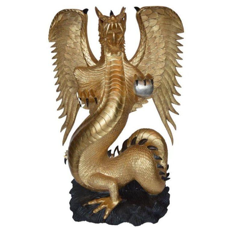 Fascinating oversized hand-carved gilt wood sculpture depicting a sturdy dragon with great detail all around. It is standing graciously on a carved black base. The orb he appears to be holding on his claw is thought to be a symbolic representation
