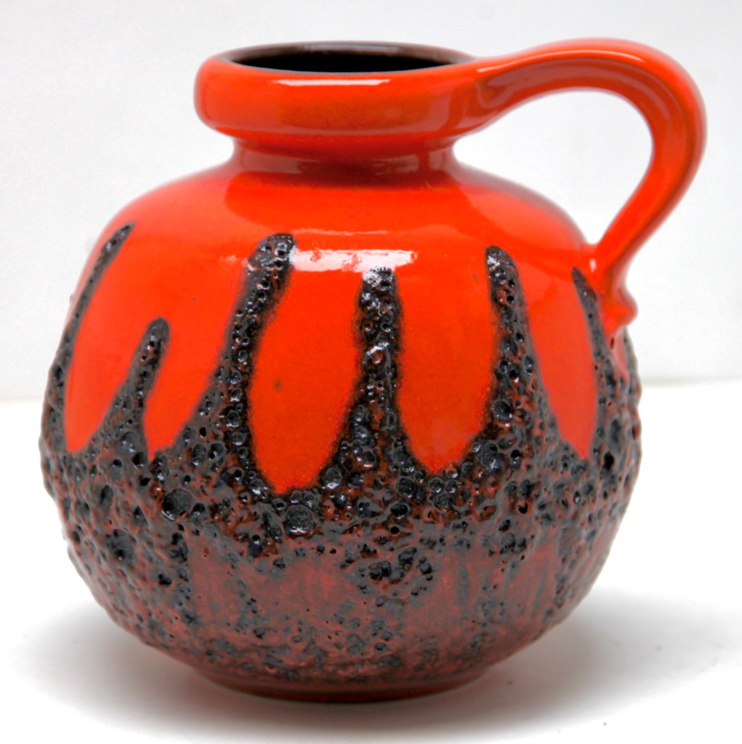 Classic fat lava red drip-glaze on charcoal background. vase with handle. 
Vintage Scheurich 
Glazed pottery.
Stamped on the base. 484-21, W-Germany.
Measures: 23 x 21 cm 
The piece is in excellent condition and a real beauty.
  
   
   