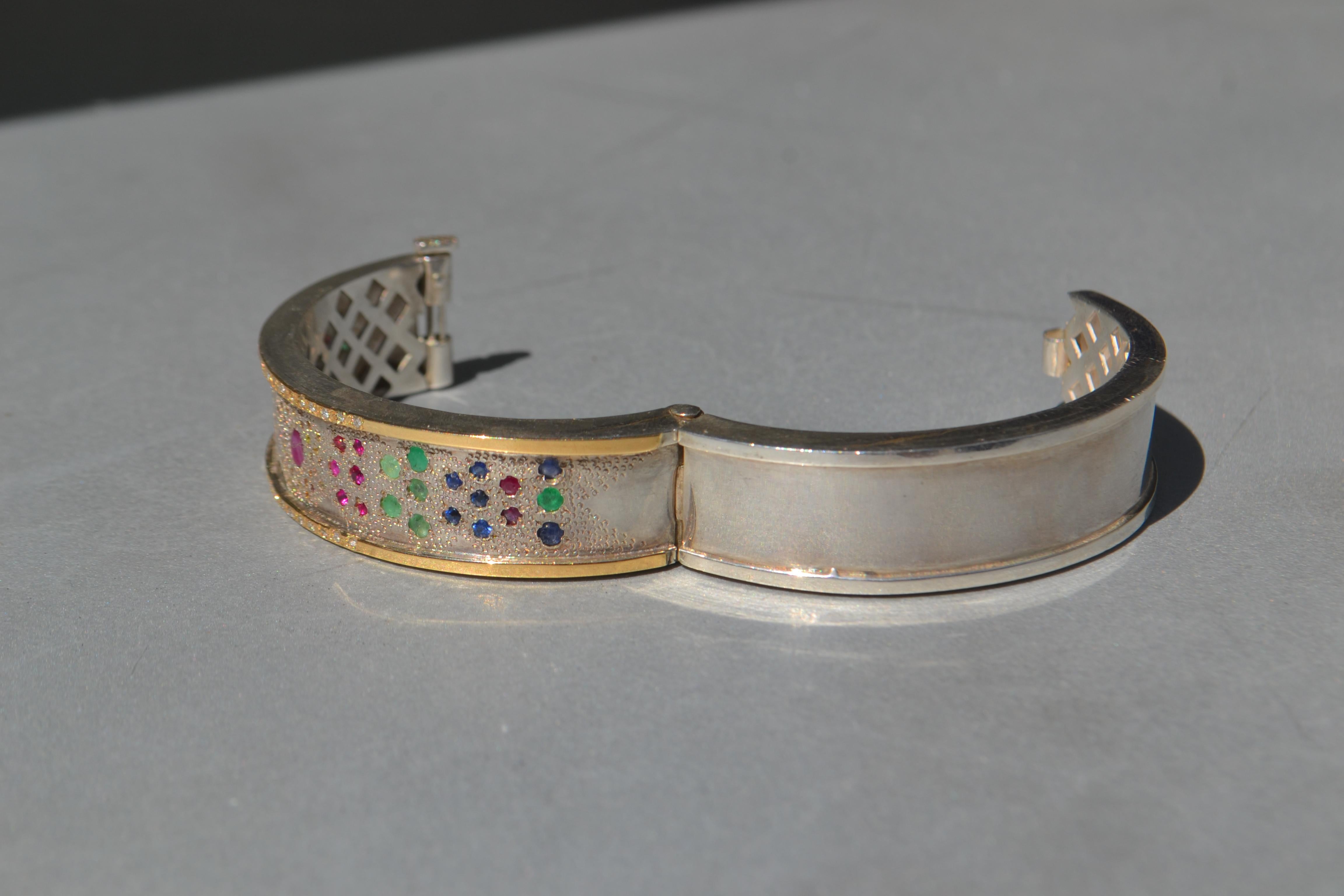 Ce bracelet est un design d'inspiration arabe avec une texture de granit dans la base, et avec une incrustation de pierres précieuses comme l'émeraude, les saphirs, les rubis, son poids est de 25 grammes entre l'or 18k et l'argent et dans les côtés