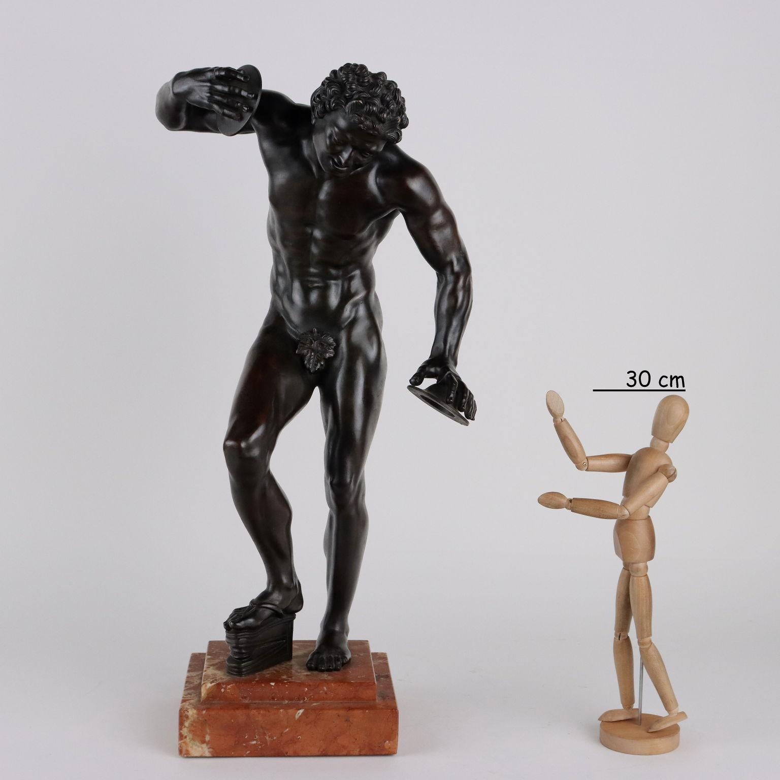 Bronze sculpture depicting faun with cymbals on red marble base.