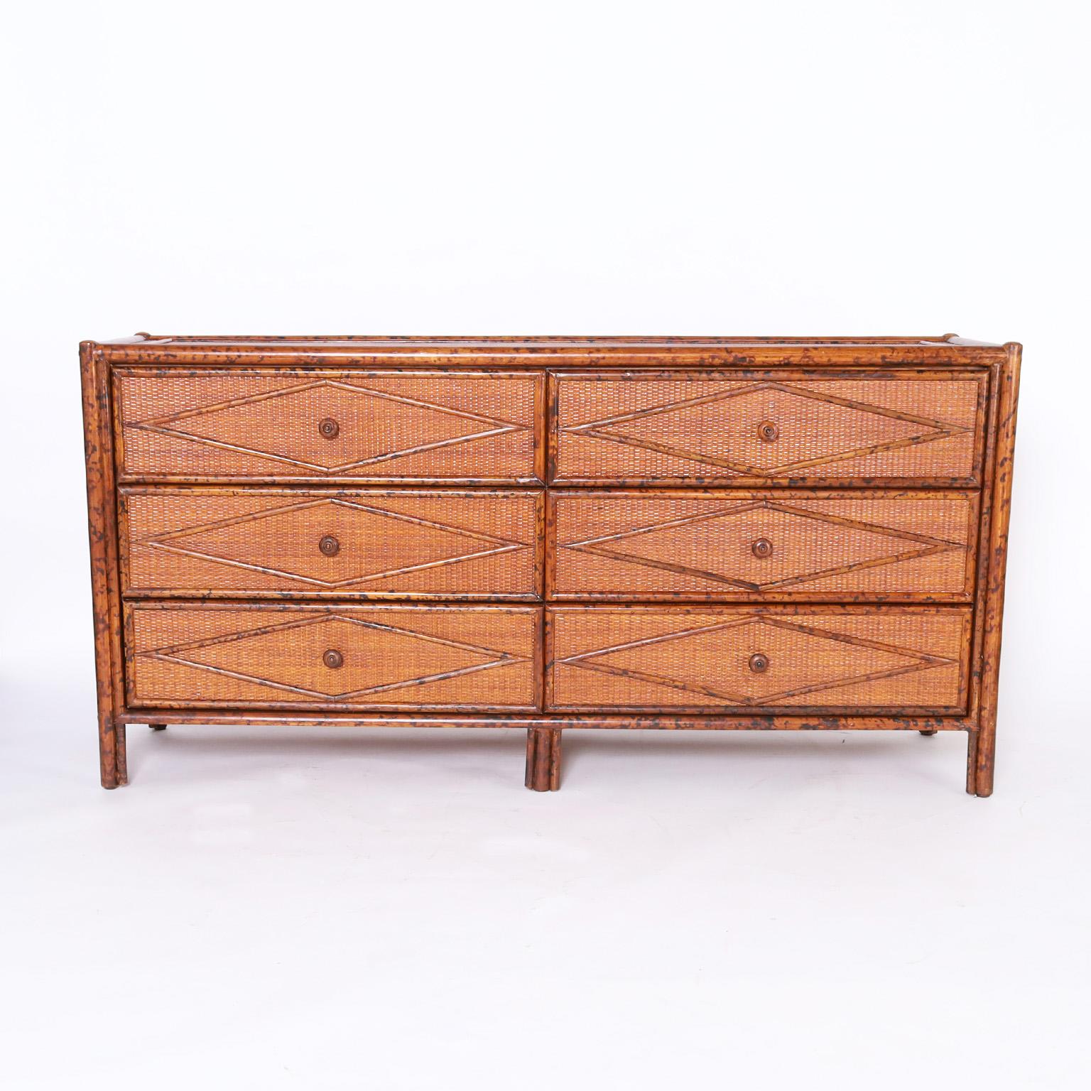 Handsome midcentury British Colonial style chest of drawers having six drawers crafted with a faux bamboo frame, grasscloth panels all around and applied geometric design in rattan.