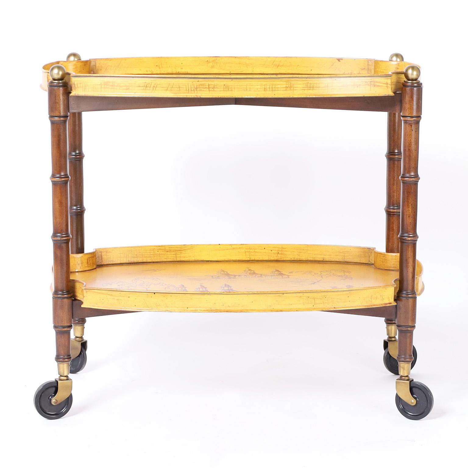 Bar cart with dynamic appeal featuring two removable tole trays decorated with chinoiserie against a mustard background. The faux bamboo frame is turned walnut with brass finials set on casters. Signed Brandt on the bottom.
