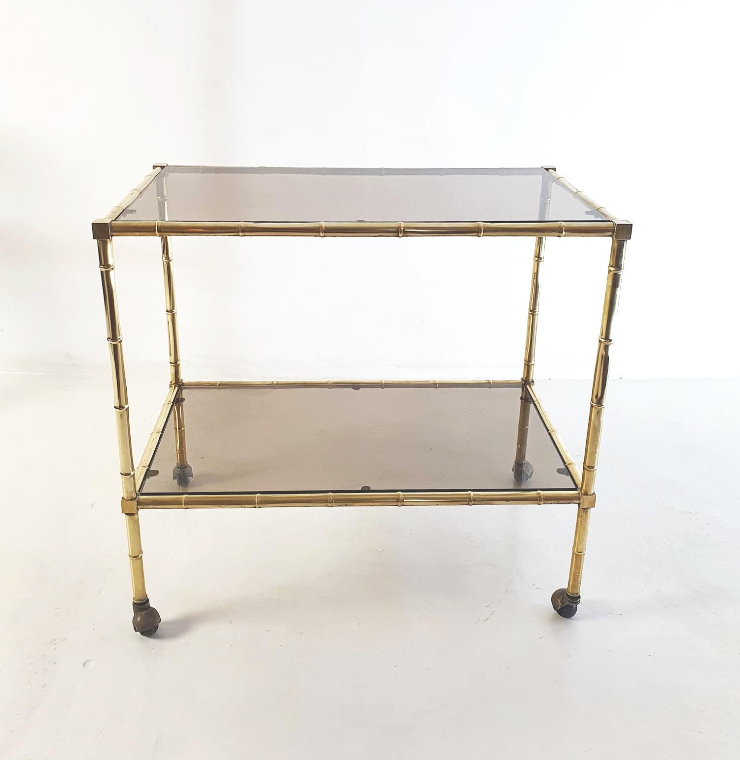 A two tiered bar cart in brass imitating bamboo and smoked glass produced during the 1970's by Maison Baguès. With original castors which works well.
Perfect as a bar or a side table.