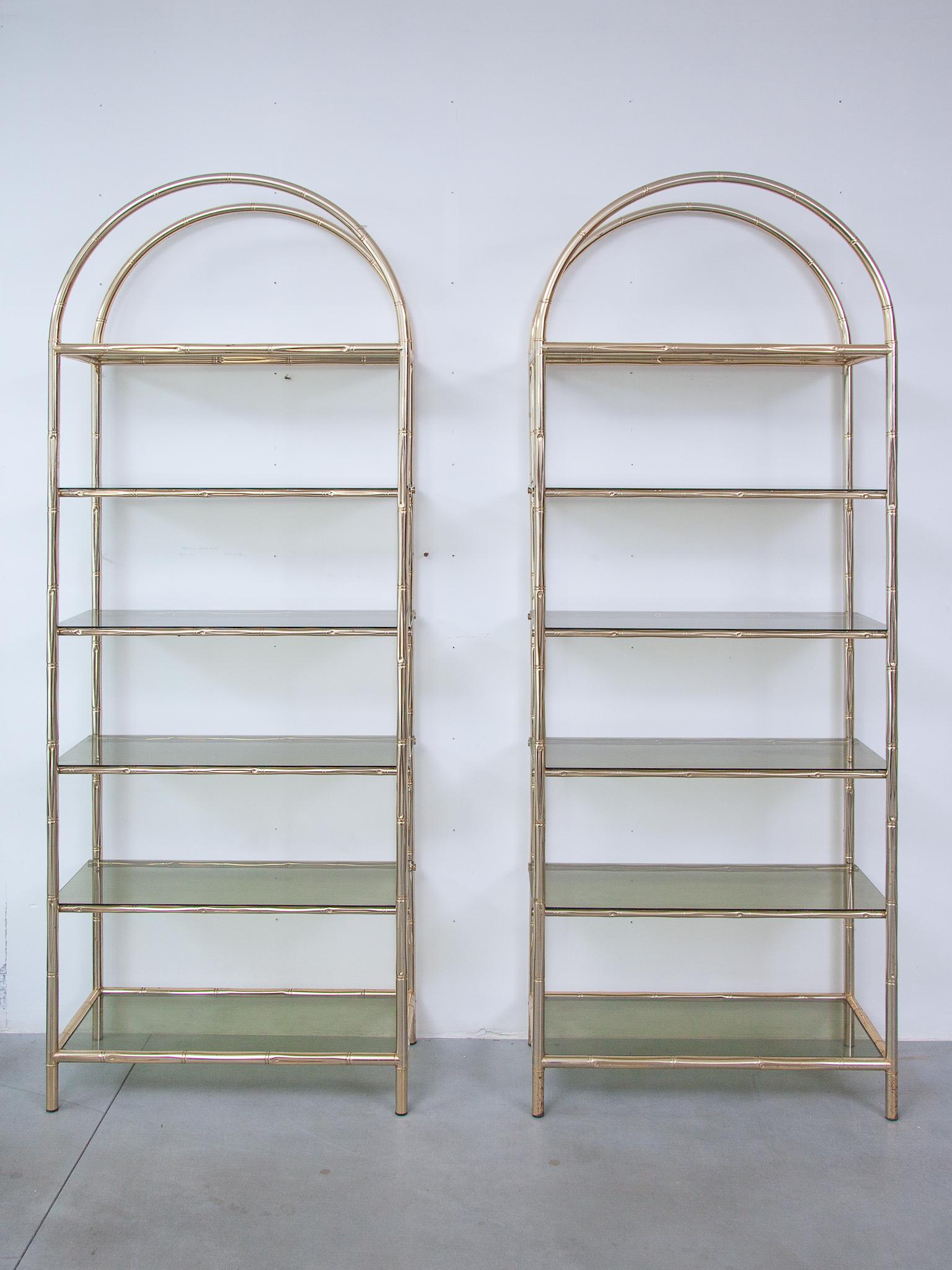 The set of two faux bamboo etageres are unique pieces of furniture that combines classic brass with a touch of nature. With sturdy legs, crafted to resemble bamboo canes, add a touch of organic charm to the piece. The fume glass shelves provides a