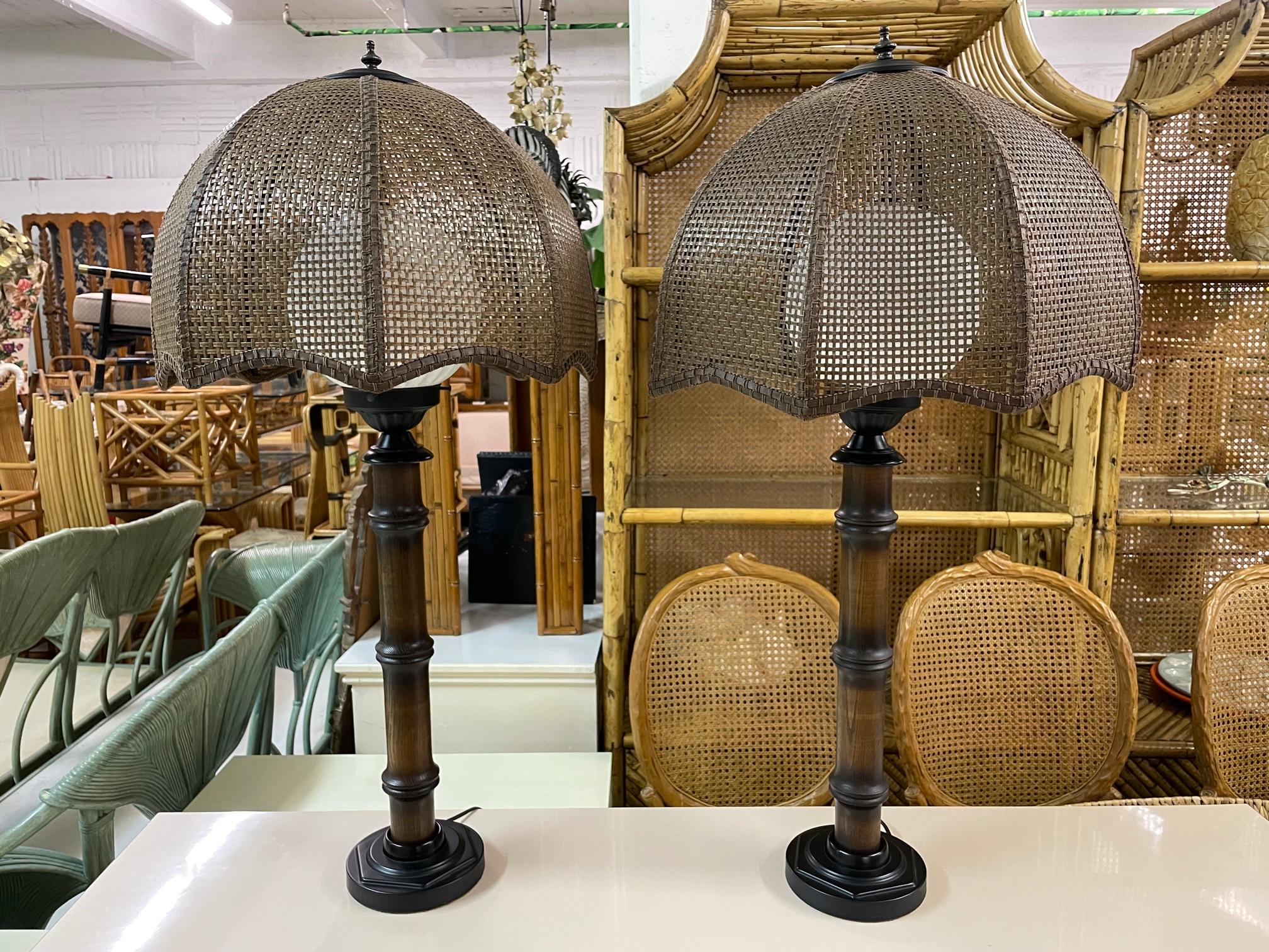 Pair of tall table lamps feature carved wood in faux bamboo style and multi-panel cane shades. Large ribbed glass globes encompass light bulbs. Excellent condition.

 