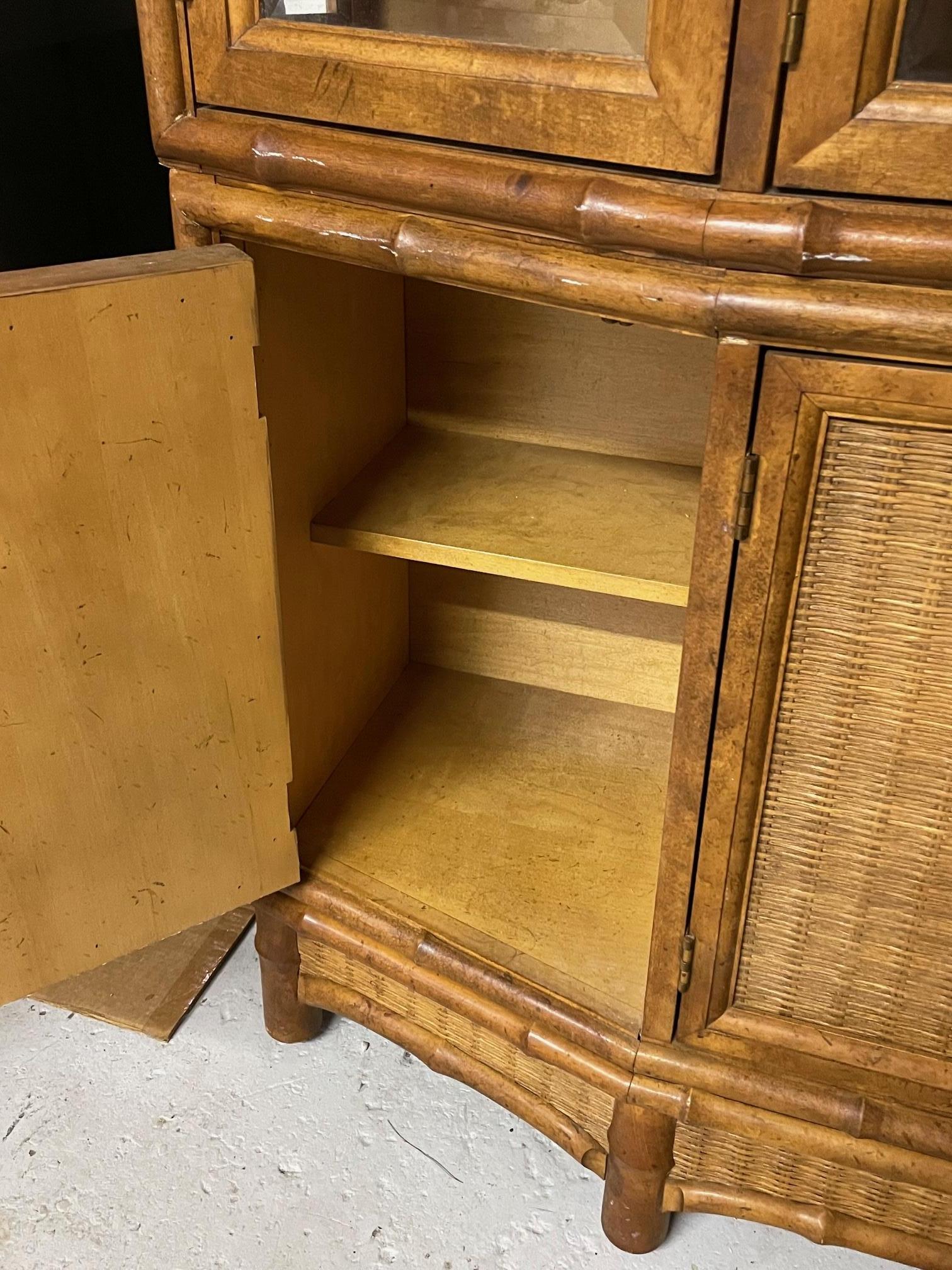 Vintage lighted china cabinet by American of Martinsville features faux bamboo detailing and wicker detailing. Four doors open to glass shelving, with storage below along with a flatware drawer. Good condition with minor imperfections consistent