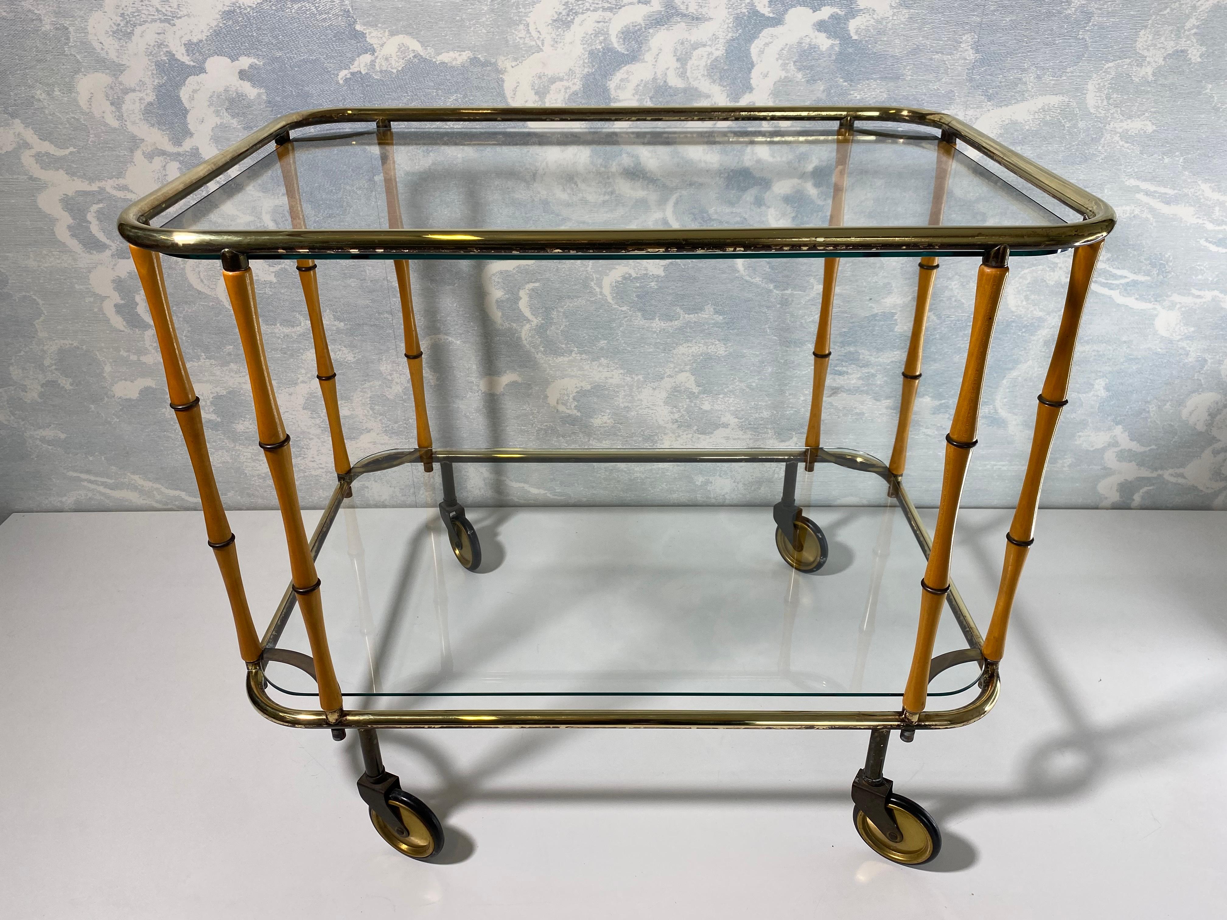 Ce superbe chariot de service à deux niveaux a très probablement été produit par l'illustre Maison Jansen en France dans les années 1960.

Quatre petites roues pivotantes soutiennent deux cadres en laiton poli séparés par huit tiges en bois