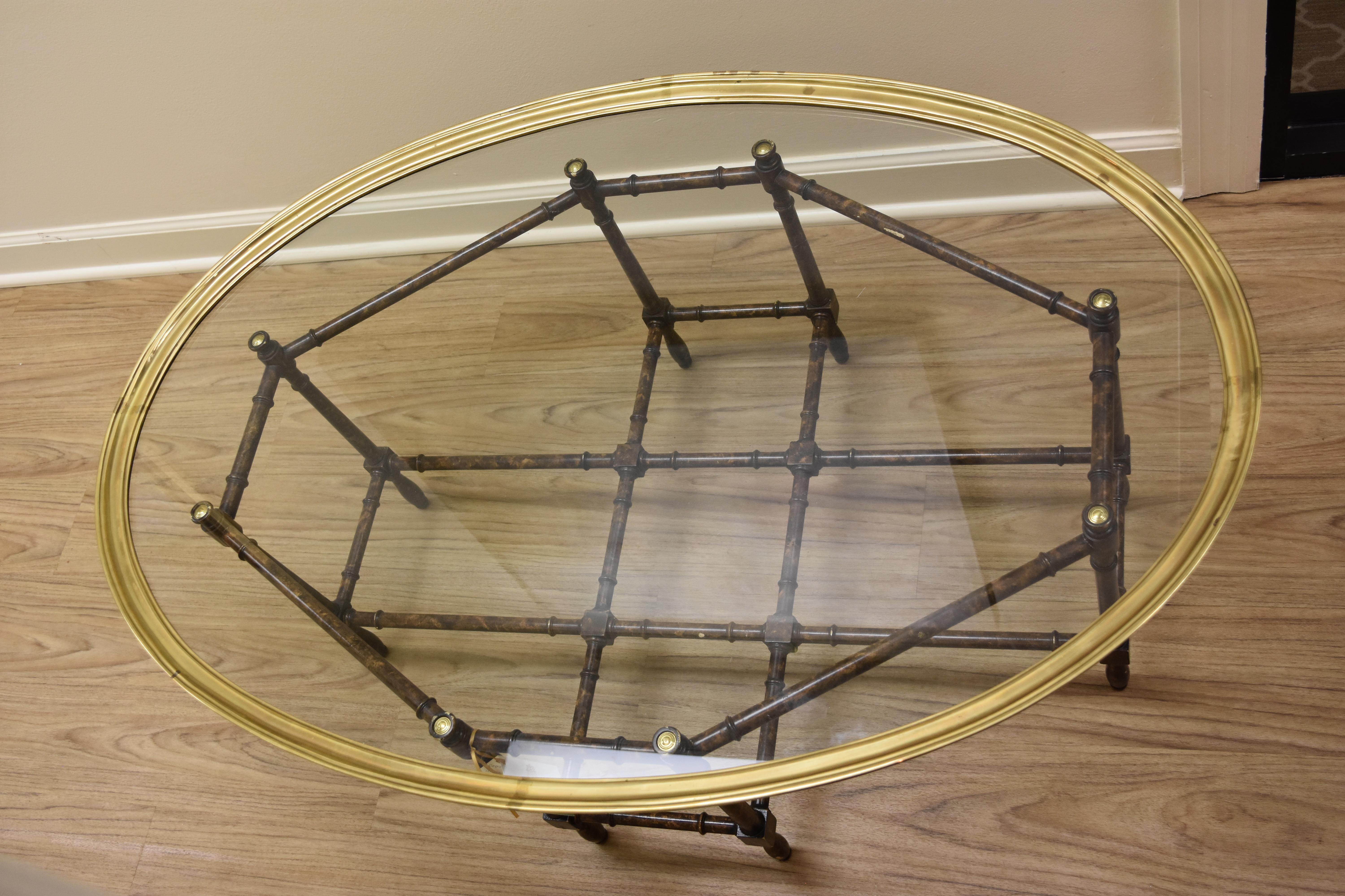 This faux bamboo coffee table is in the Hollywood Regency style and was likely made by Baker. It has a faux bamboo base made out of a resin type material with a tortoise looking finish. The brass and glass top lifts off for easy cleaning and
